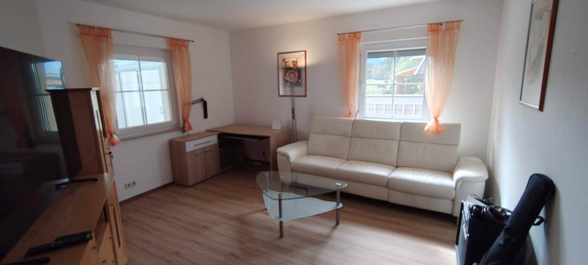 Gemütliches Wohnzimmer mit hellem Sofa, Holzfußboden und Schreibtischbereich.