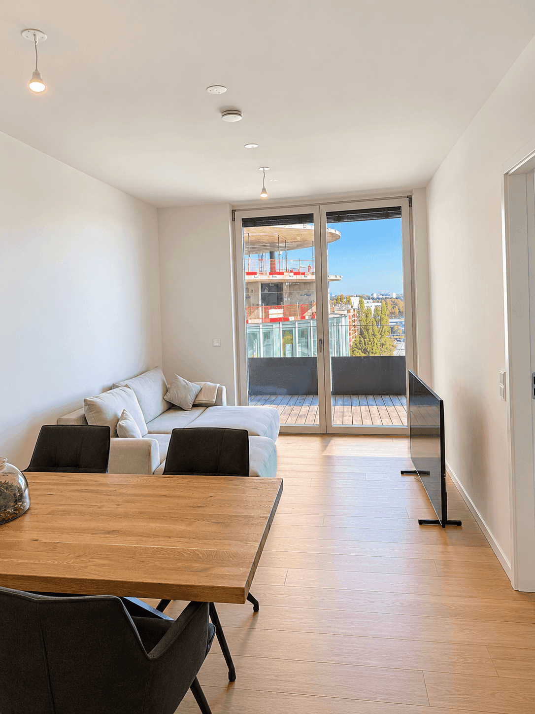 Heller Wohn- und Essbereich mit Holzboden, Sofa und Zugang zum Balkon.