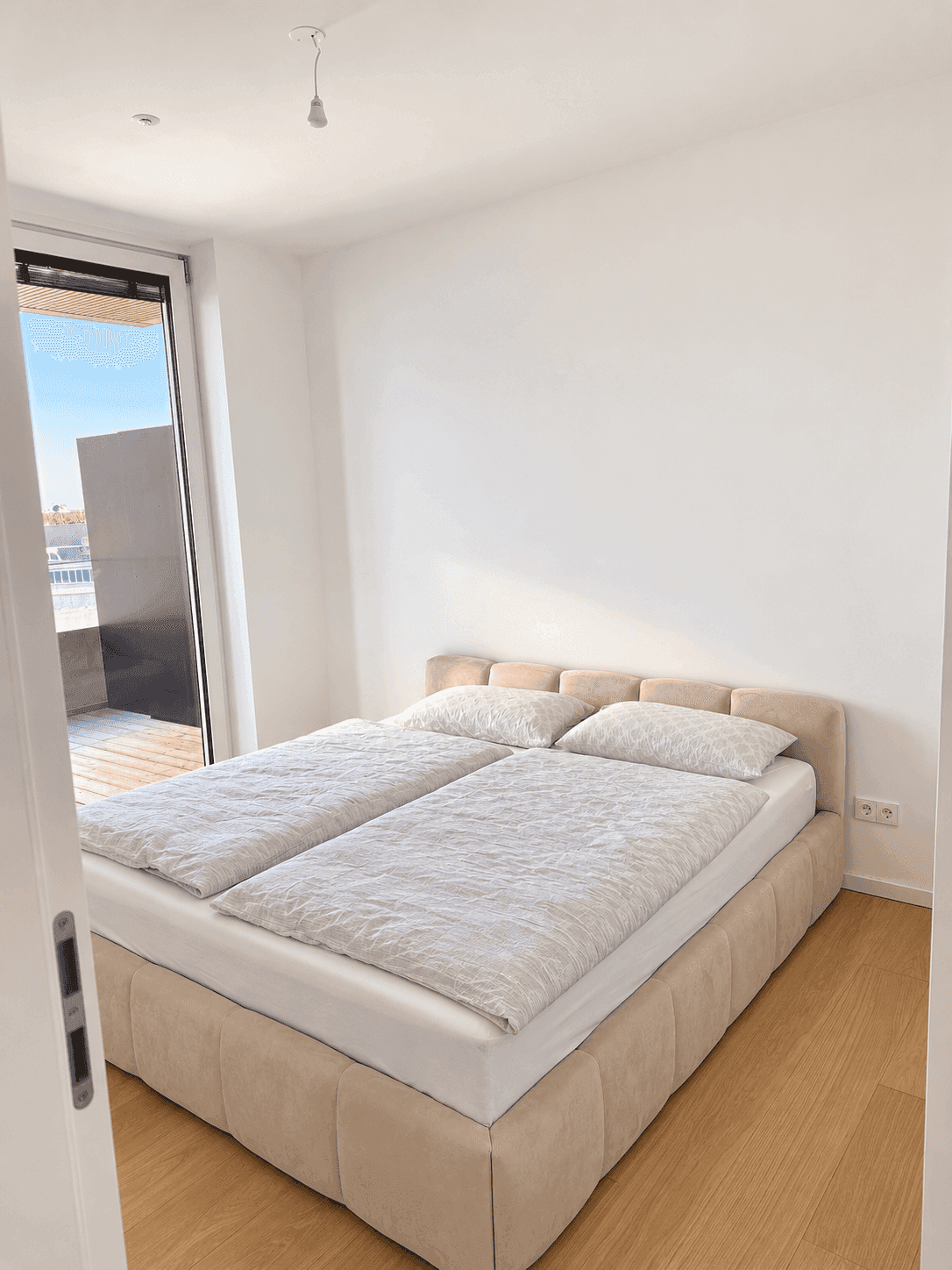Helles Schlafzimmer mit Doppelbett, Holzboden und Zugang zu einem Balkon.