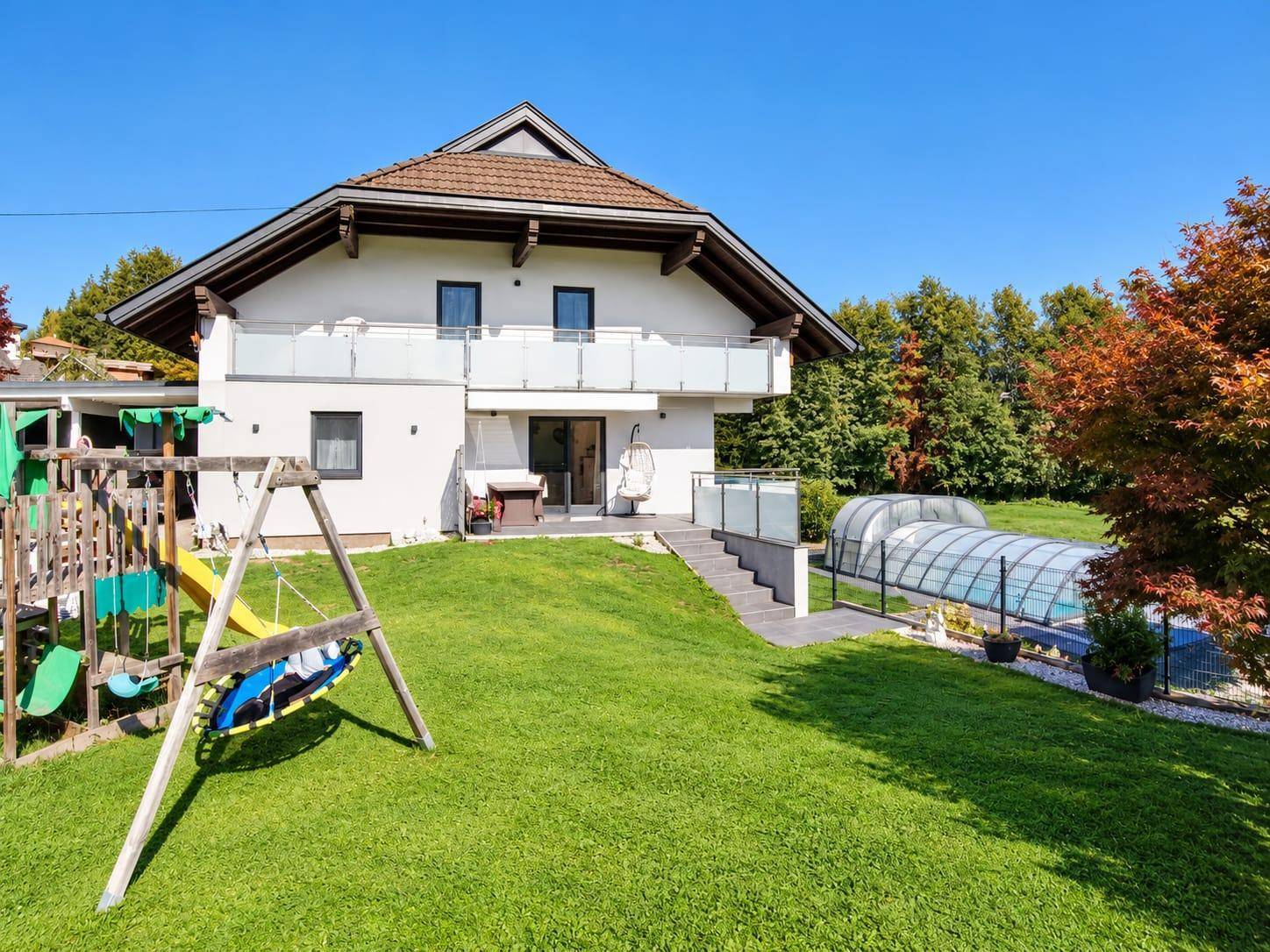 Familienfreundlicher Garten mit Spielplatz und Schaukeln neben dem modernen Wohnhaus und einer Terrasse.