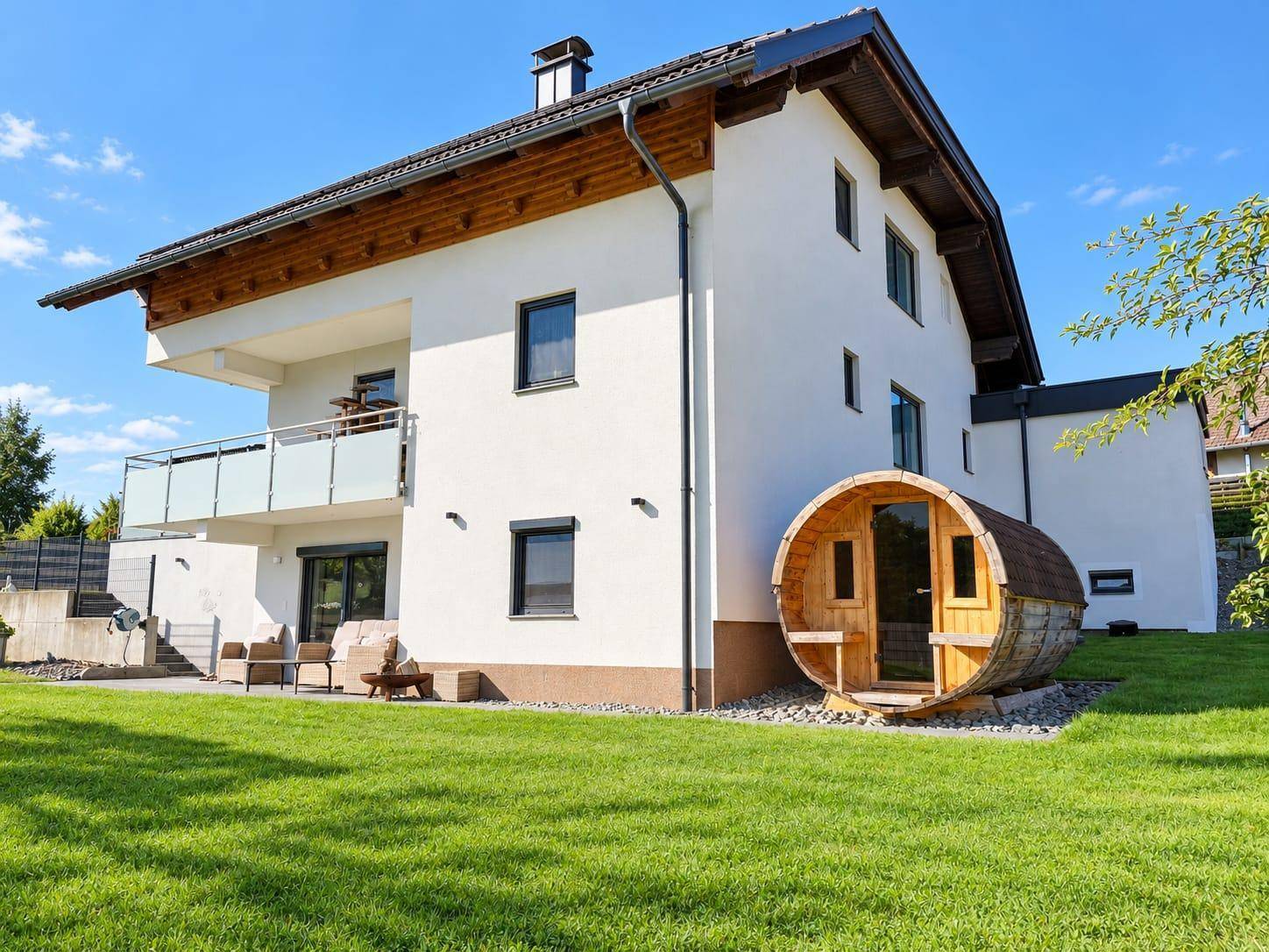 Modernes Wohnhaus mit großem Garten und einer freistehenden Fasssauna im Grünen.