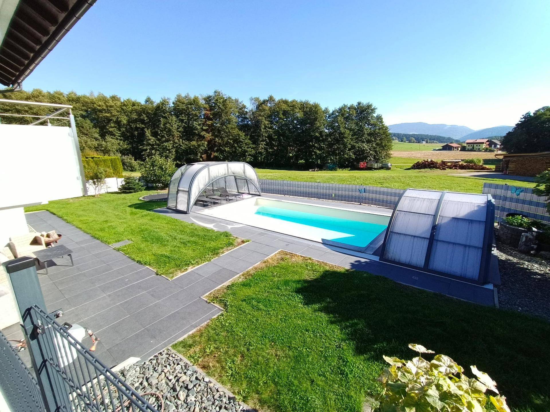 Großer überdachter Pool im Garten mit weitem Blick auf die umliegende Landschaft und grüne Felder.