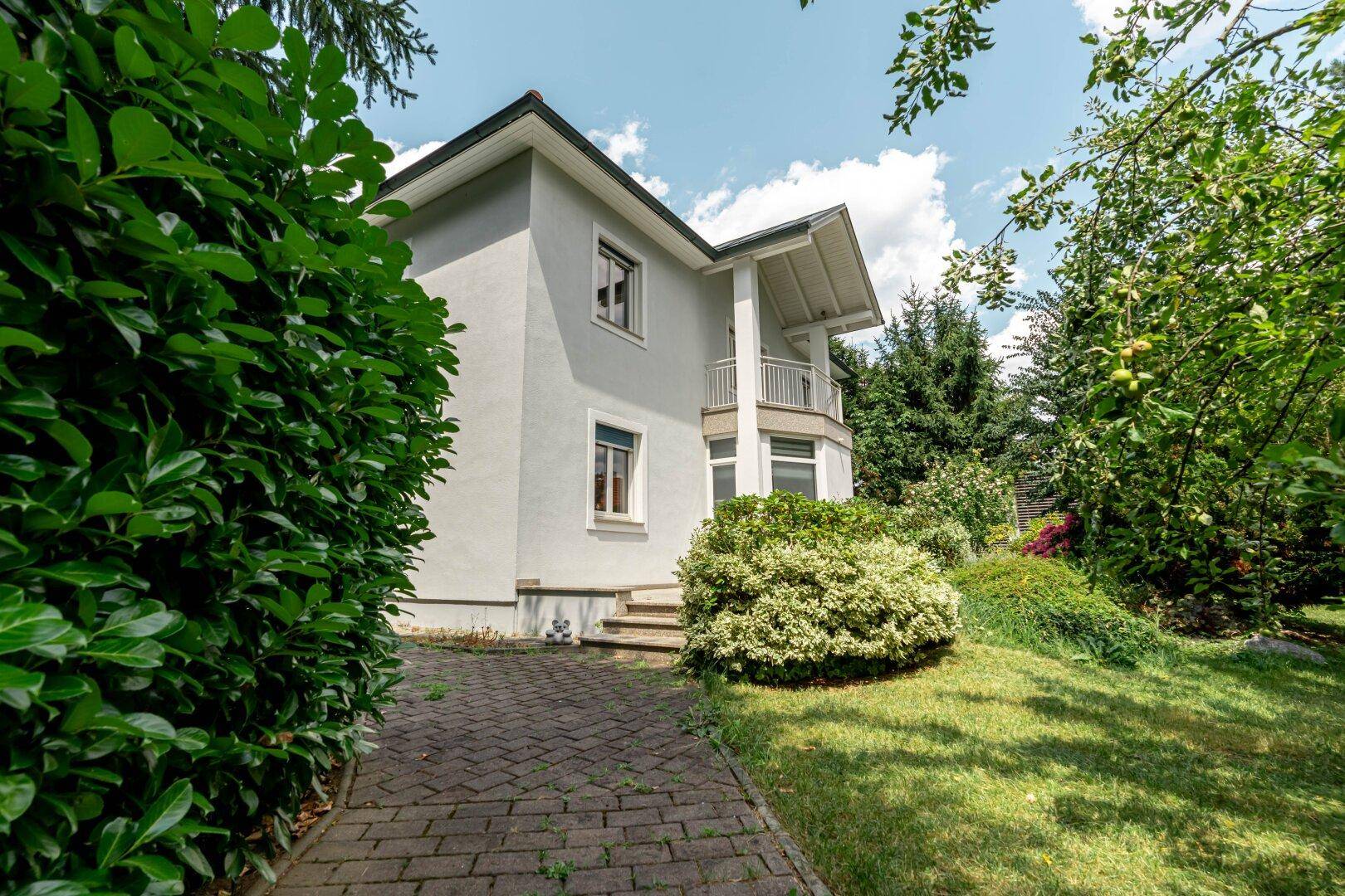 Seitlicher Blick auf das Haus mit gepflegtem Garten, Rasenfläche und üppiger Bepflanzung.