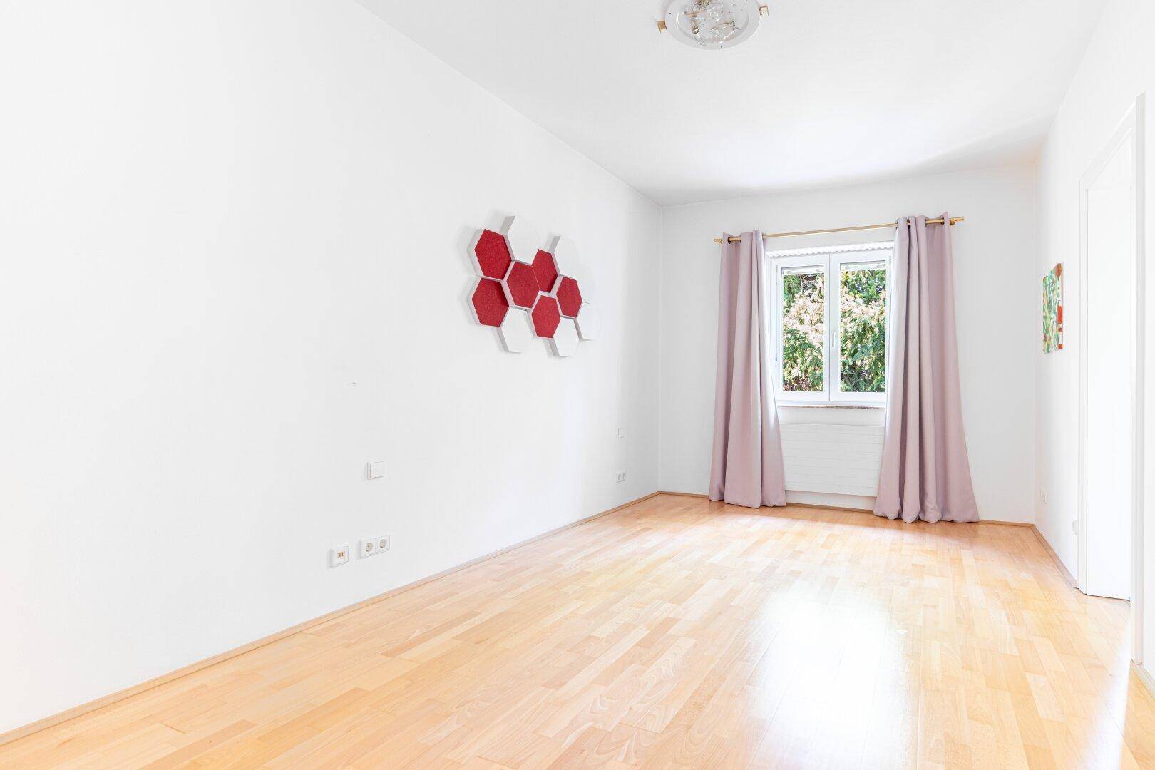 Helles Schlafzimmer mit Holzboden, weißen Wänden und einem Fenster mit rosa Vorhängen, bietet eine freundliche Atmosphäre.