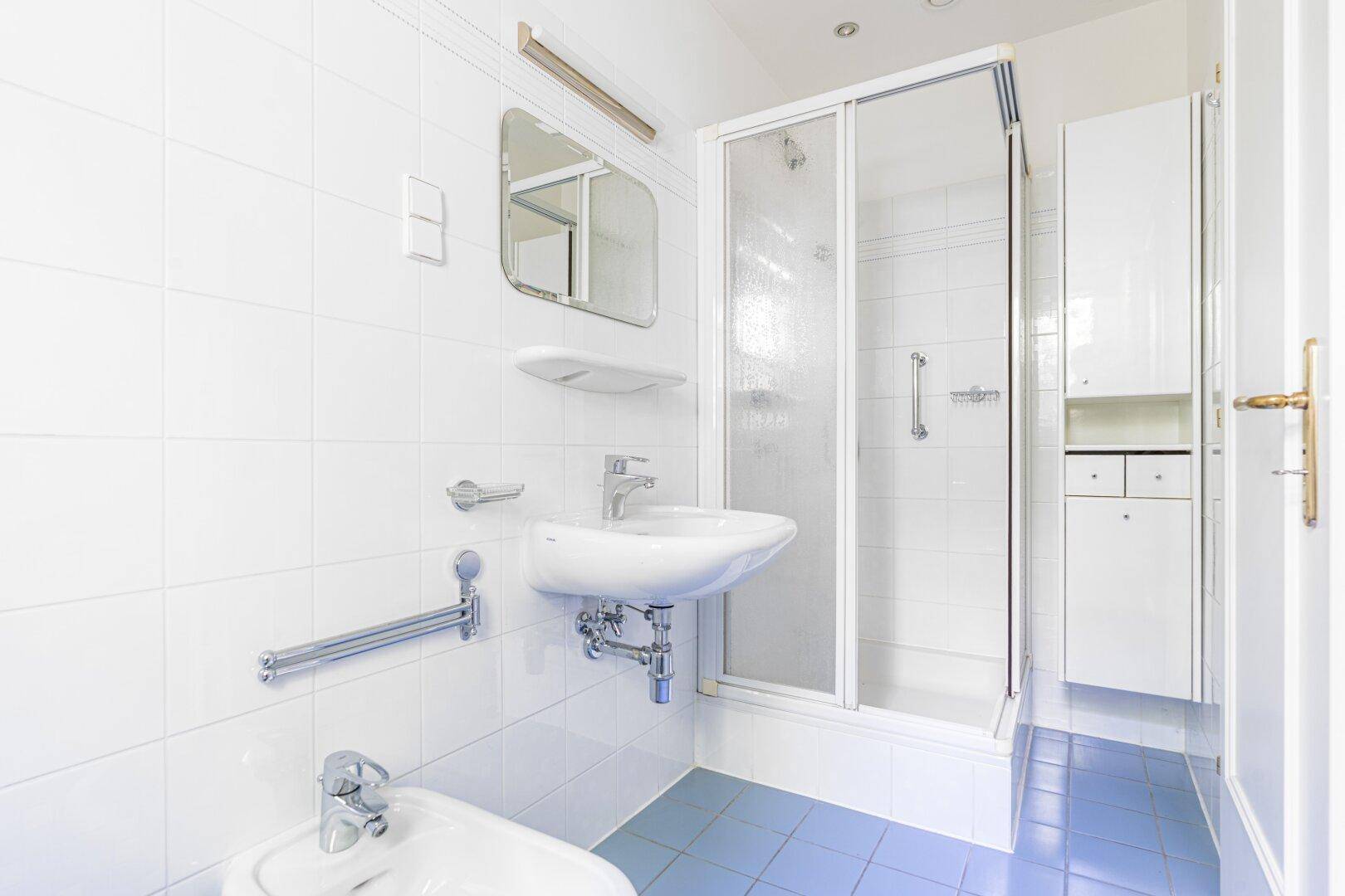Funktionales Badezimmer mit blauen Bodenfliesen, weiß gefliesten Wänden und einer Duschkabine.