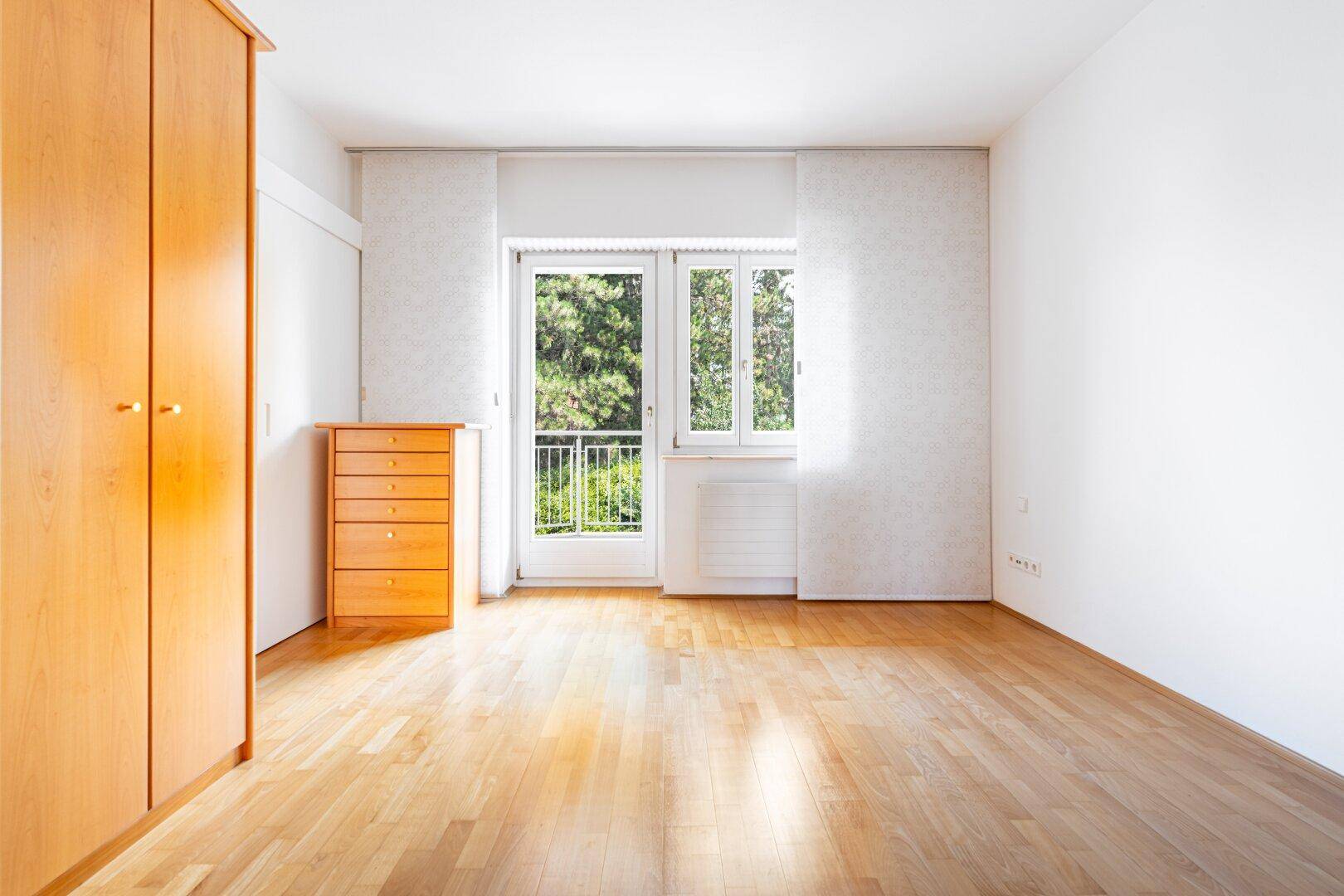 Geräumiges Schlafzimmer mit hellem Holzboden, weiß gestrichenen Wänden und einem französischen Balkon.