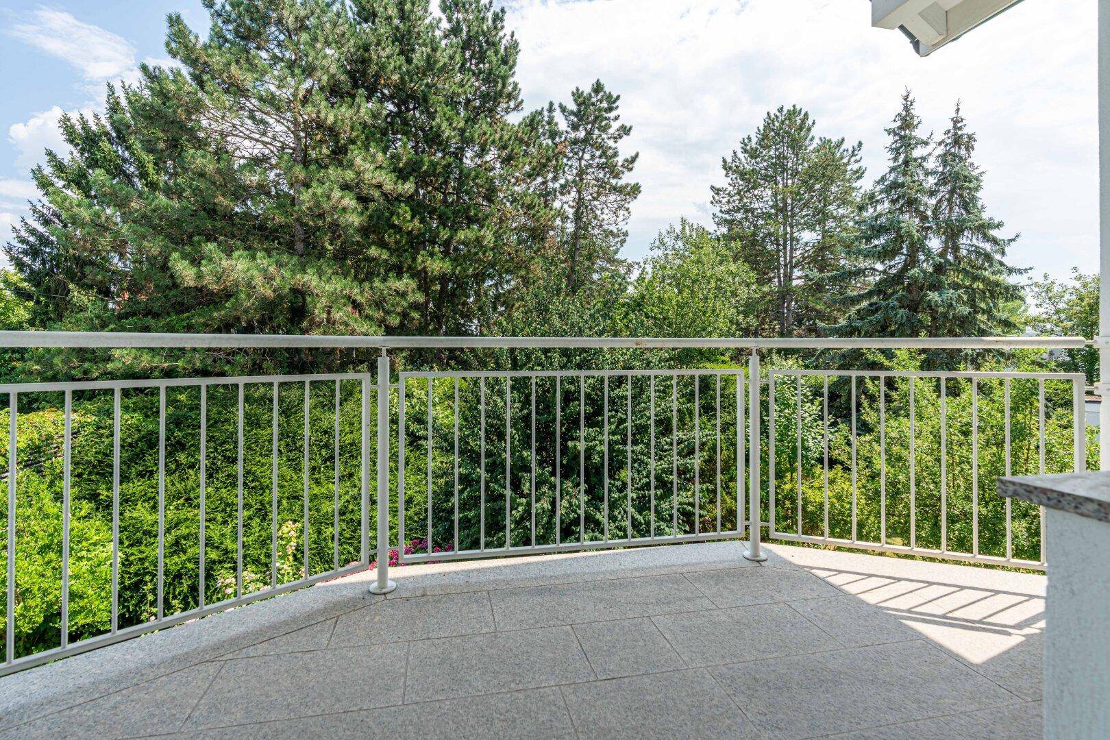 Großer Balkon mit Fliesenboden und Metallgeländer, bietet einen weiten Blick auf die umliegende grüne Landschaft.