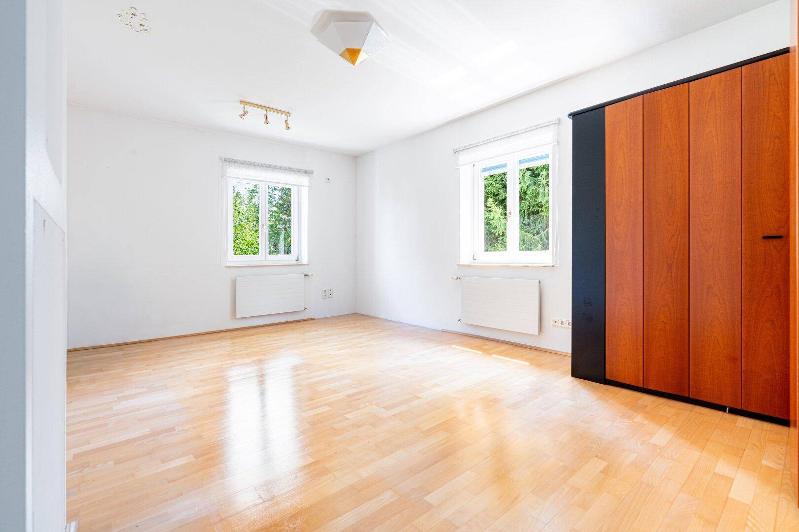 Helles Schlafzimmer mit Holzboden und großem Kleiderschrank, bietet viel Platz und Tageslicht durch die Fenster.