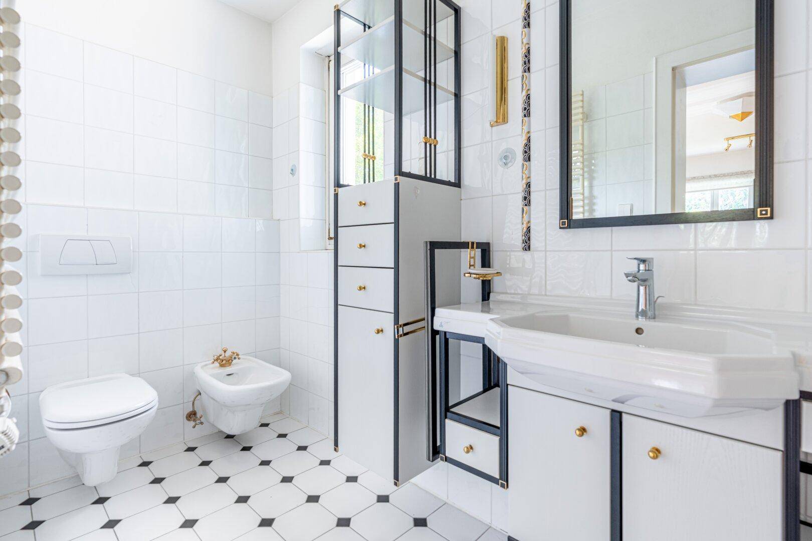 Elegantes Badezimmer mit schwarz-weißen Fliesen, Bidet, WC und einem stilvollen Waschtisch mit goldenen Akzenten.
