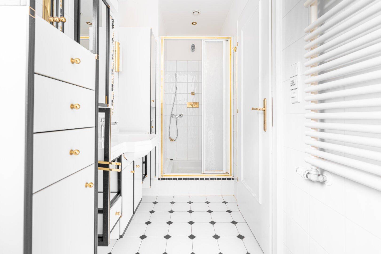 Modernes Badezimmer mit schwarz-weißen Fliesen, Dusche und stilvollen goldenen Armaturen und Details.