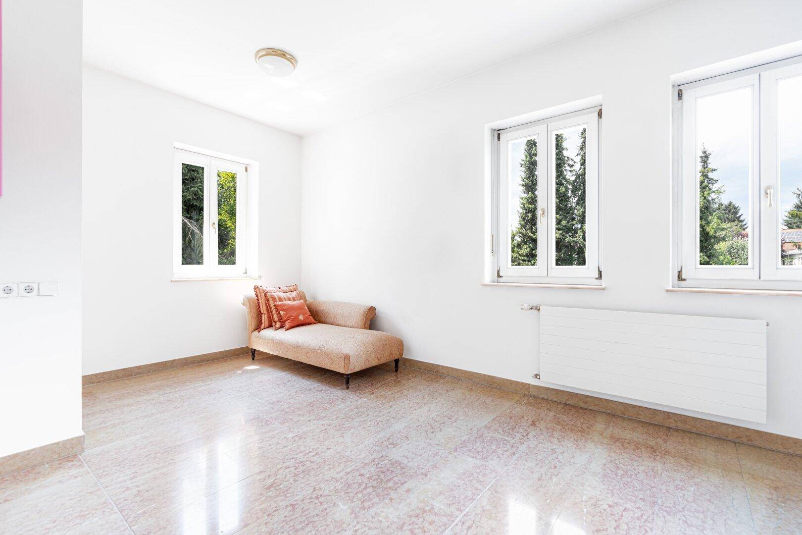 Lichtdurchfluteter Raum mit Terrazzoboden, großen Fenstern und einem beigen Chaiselongue, ideal zum Entspannen.