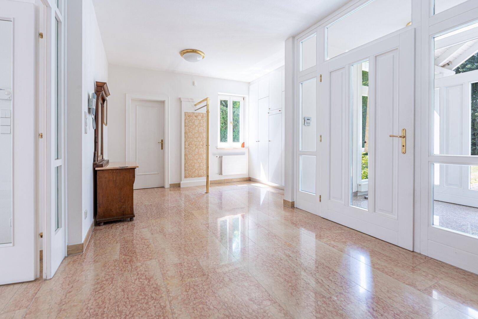 Geräumiger Flur mit glänzenden Terrazzofliesen, weiß gestrichenen Wänden und einem klassischen Holzschrank.