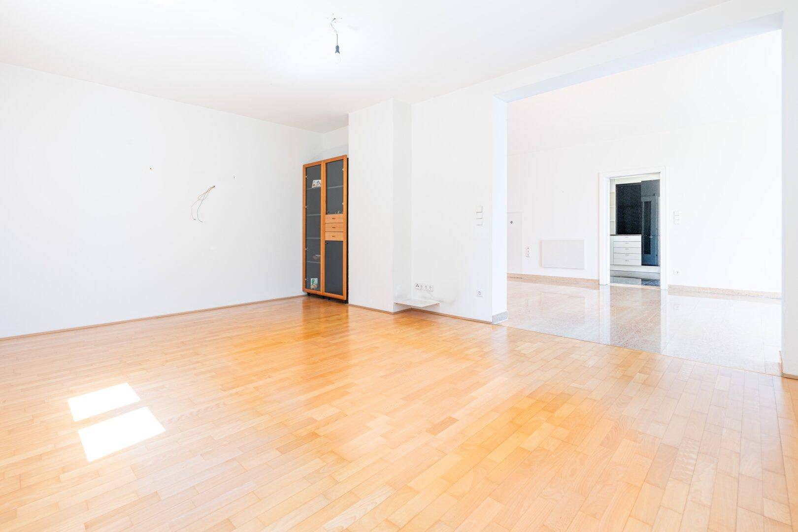 Geräumiges Wohnzimmer mit hellem Parkettboden und weiß gestrichenen Wänden, bietet viel Platz für Gestaltung.