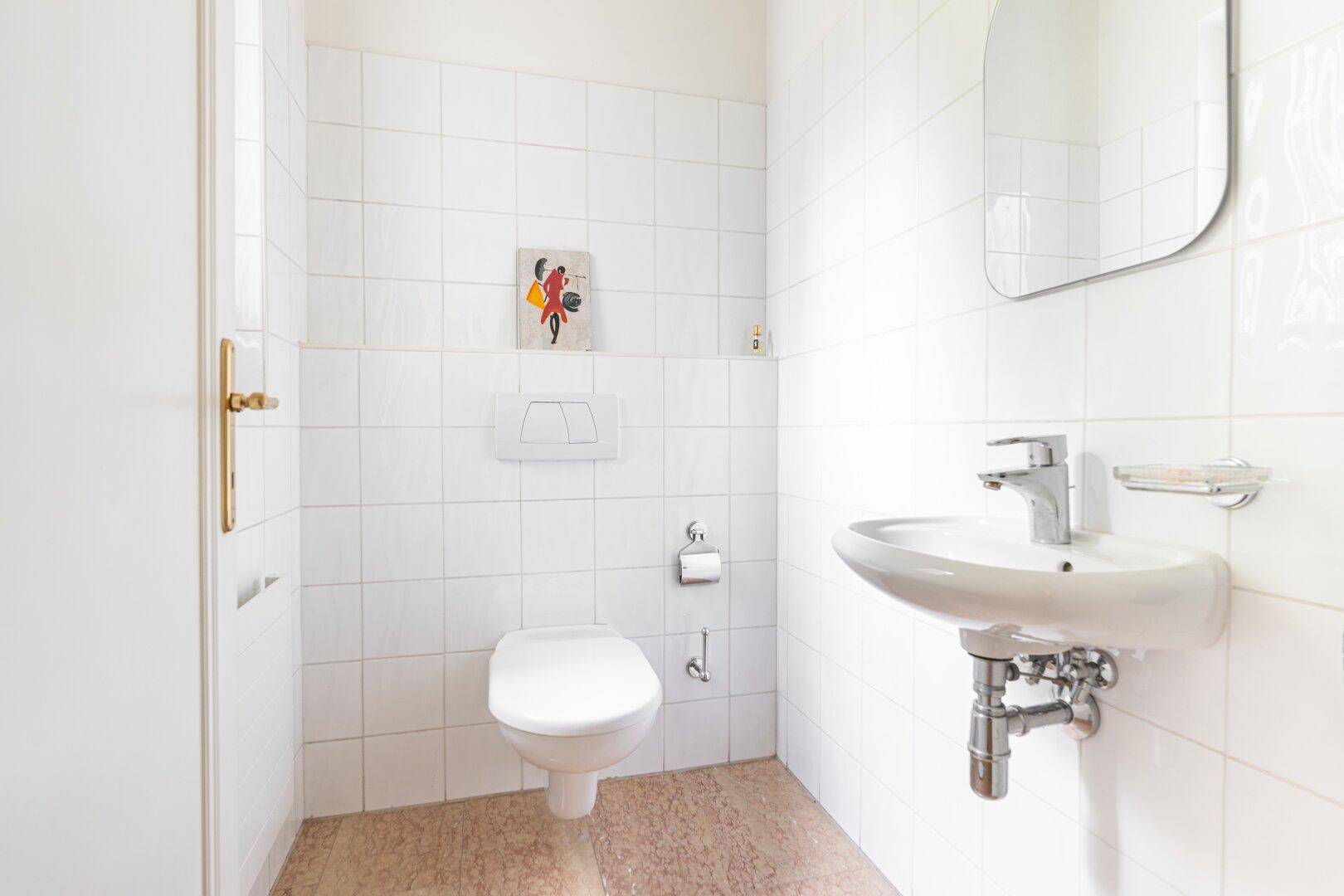 Kleines Gäste-WC mit weiß gefliesten Wänden, Terrazzoboden und einem einfachen Waschbecken.