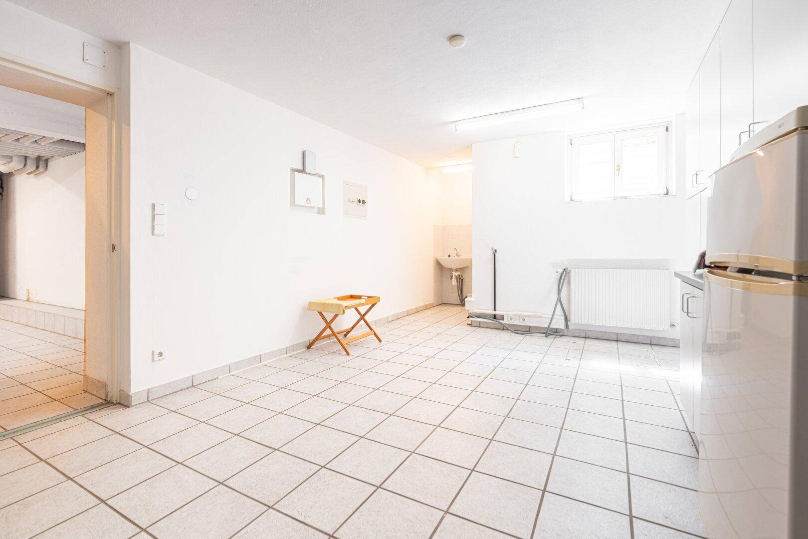 Heller Hauswirtschaftsraum mit Fliesenboden, Waschbecken und Stauraum, ideal für Wäsche und Lagerung.