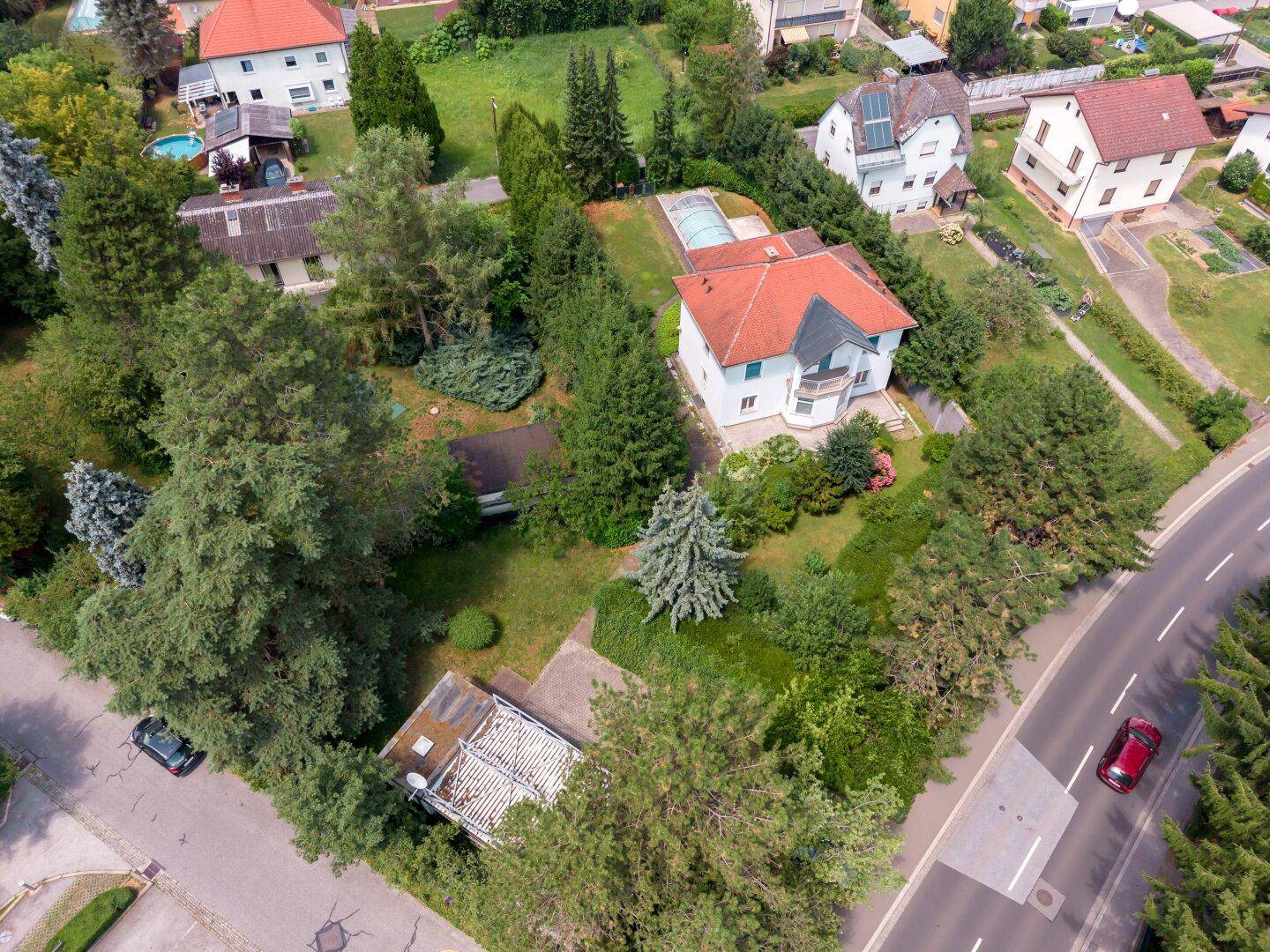 Luftaufnahme eines Einfamilienhauses mit großem Garten, umgeben von weiteren Wohnhäusern und viel Grün.