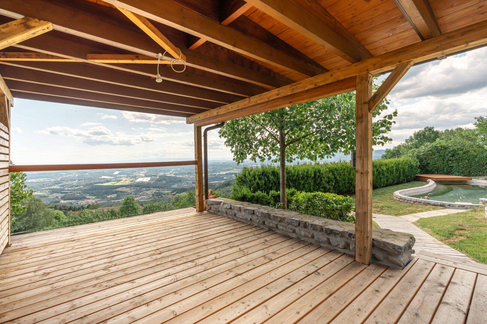 Große überdachte Holzterrasse mit Panoramablick über die weite Landschaft und den Poolbereich.