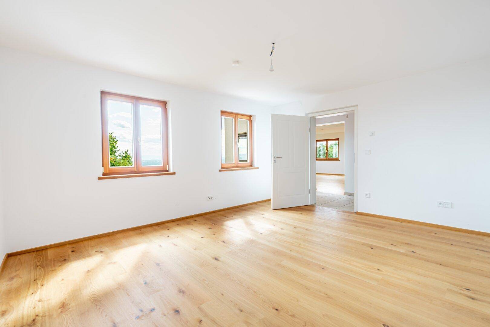 Helles Zimmer mit Holzboden und zwei Fenstern, die einen schönen Blick auf die Umgebung bieten.