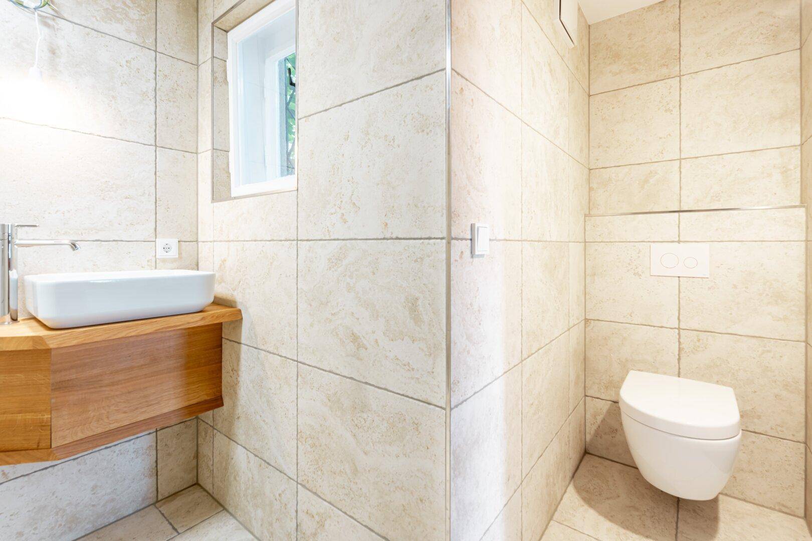 Modernes Gäste-WC mit beigefarbenen Fliesen, wandhängendem WC und einem kleinen Fenster.