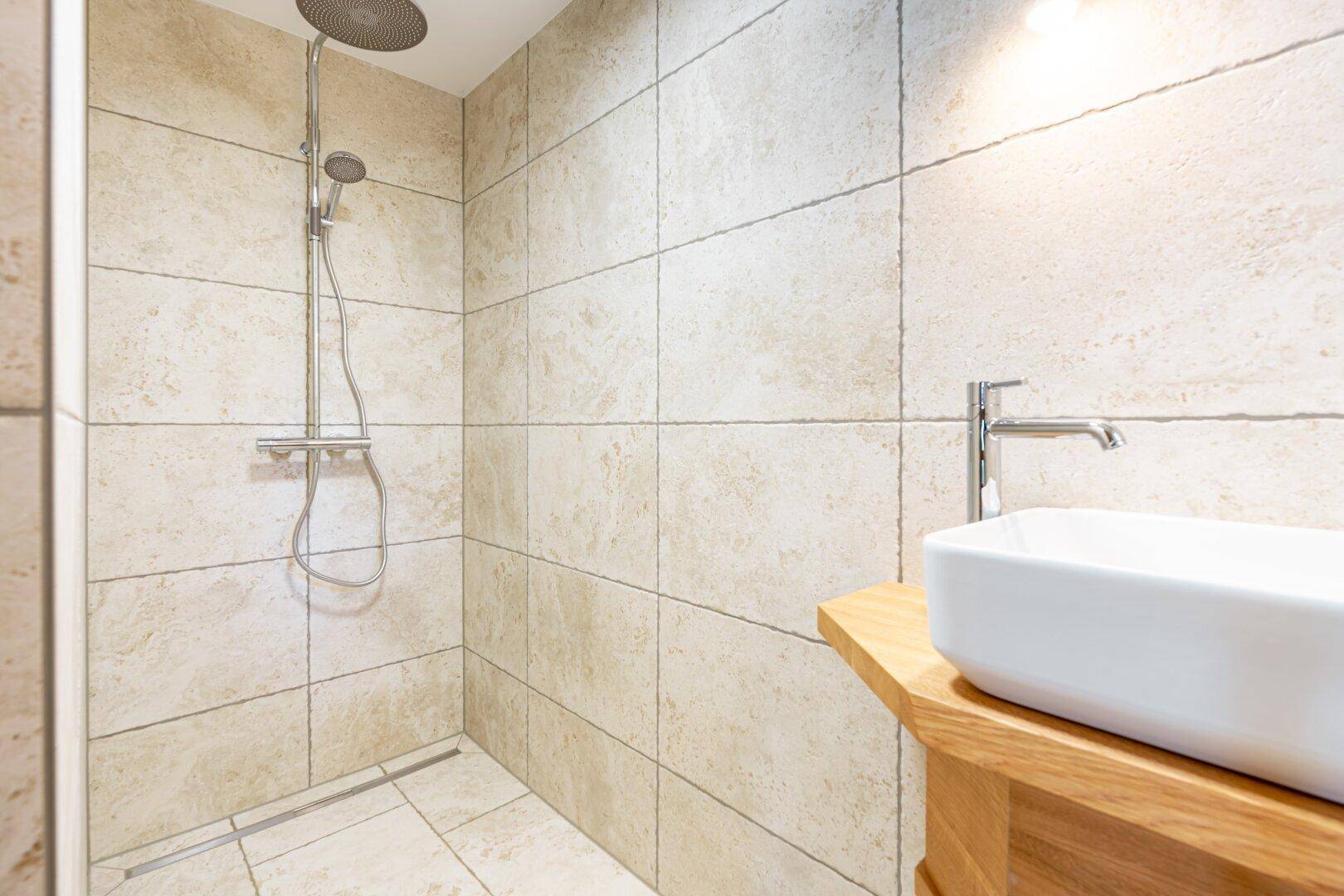 Modernes Badezimmer mit beigefarbenen Fliesen, ebenerdiger Dusche und stilvollem Waschbecken.