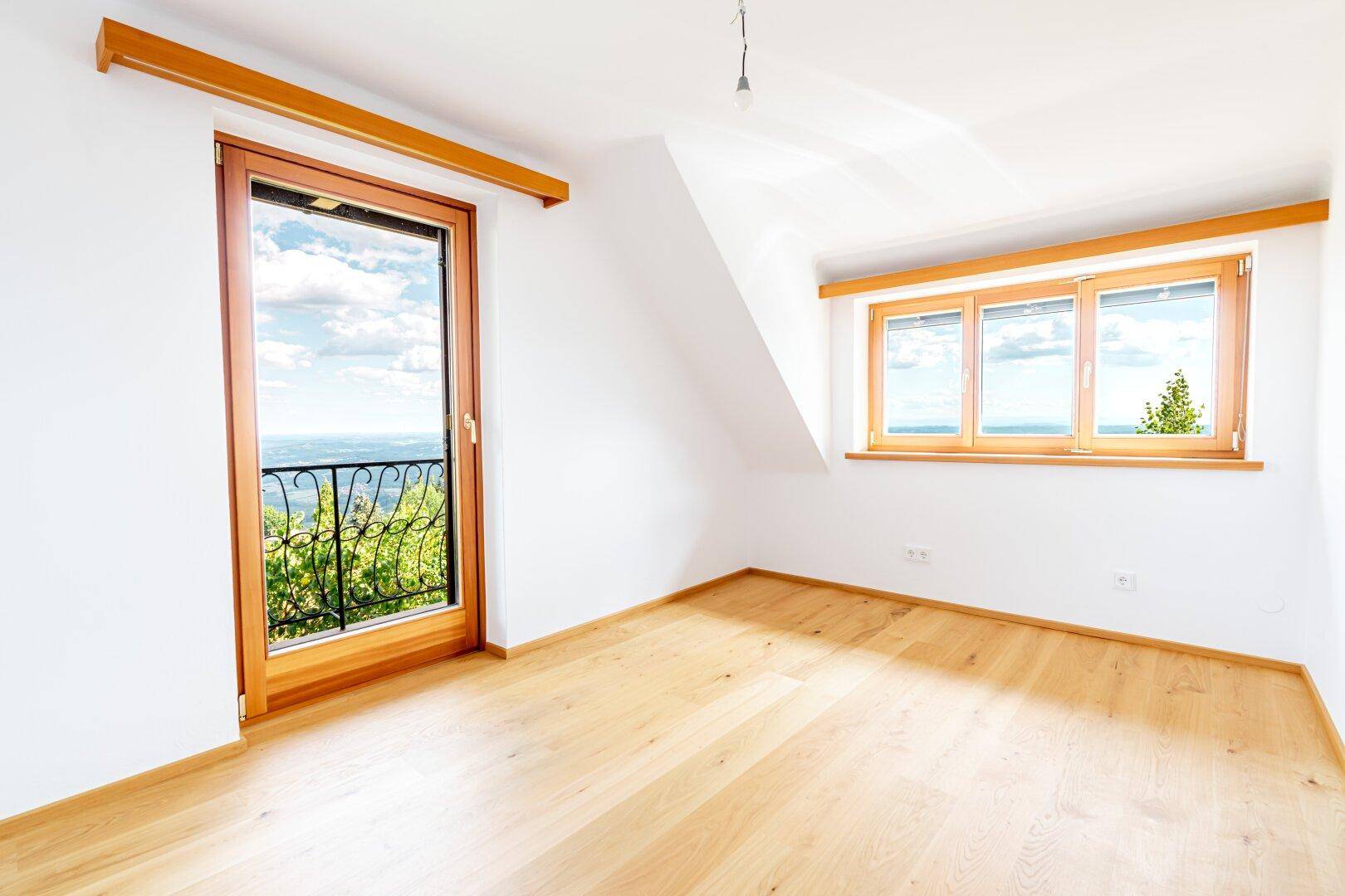 Helles Schlafzimmer mit Holzboden und Zugang zu einem französischen Balkon mit weitem Blick.