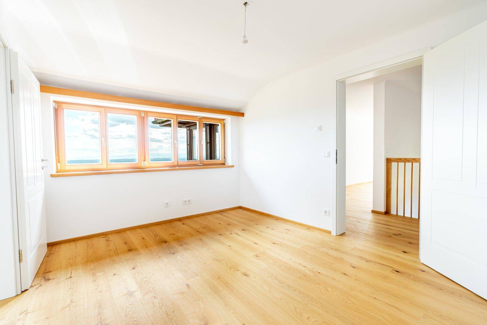 Geräumiges, helles Zimmer mit Holzboden und großen Fenstern, ideal als Schlaf- oder Arbeitszimmer.