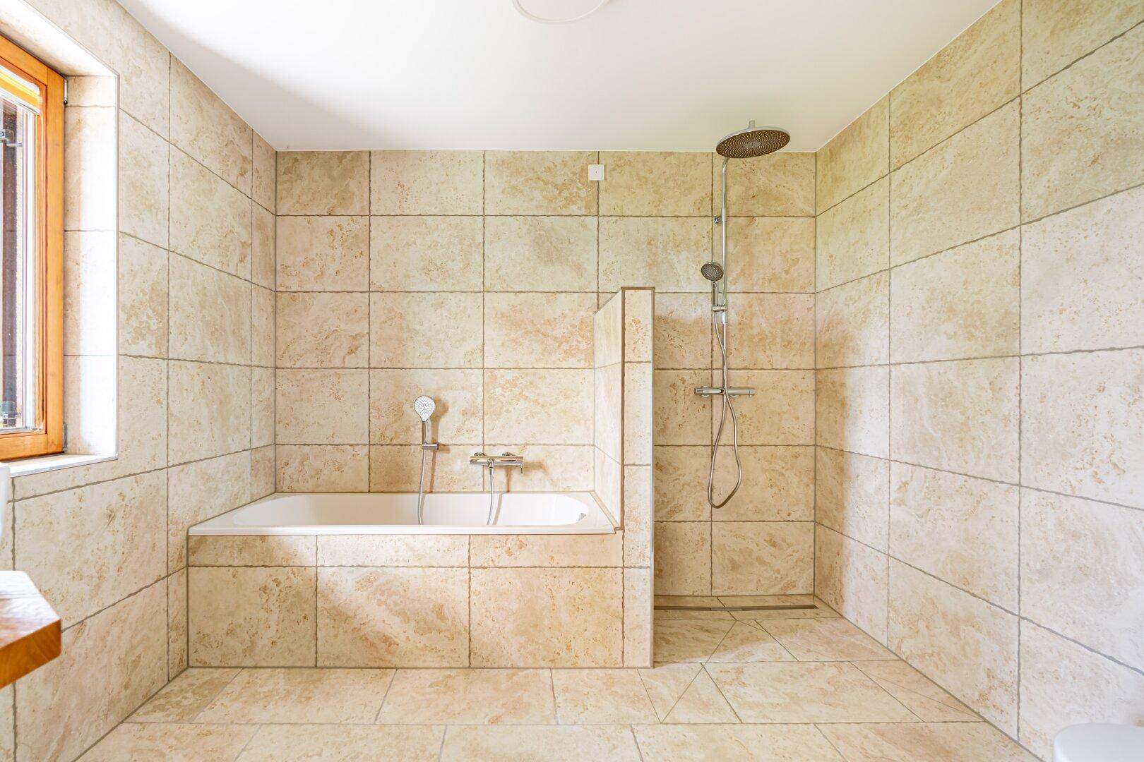 Geräumiges Badezimmer mit beigefarbenen Fliesen, Badewanne und ebenerdiger Dusche.