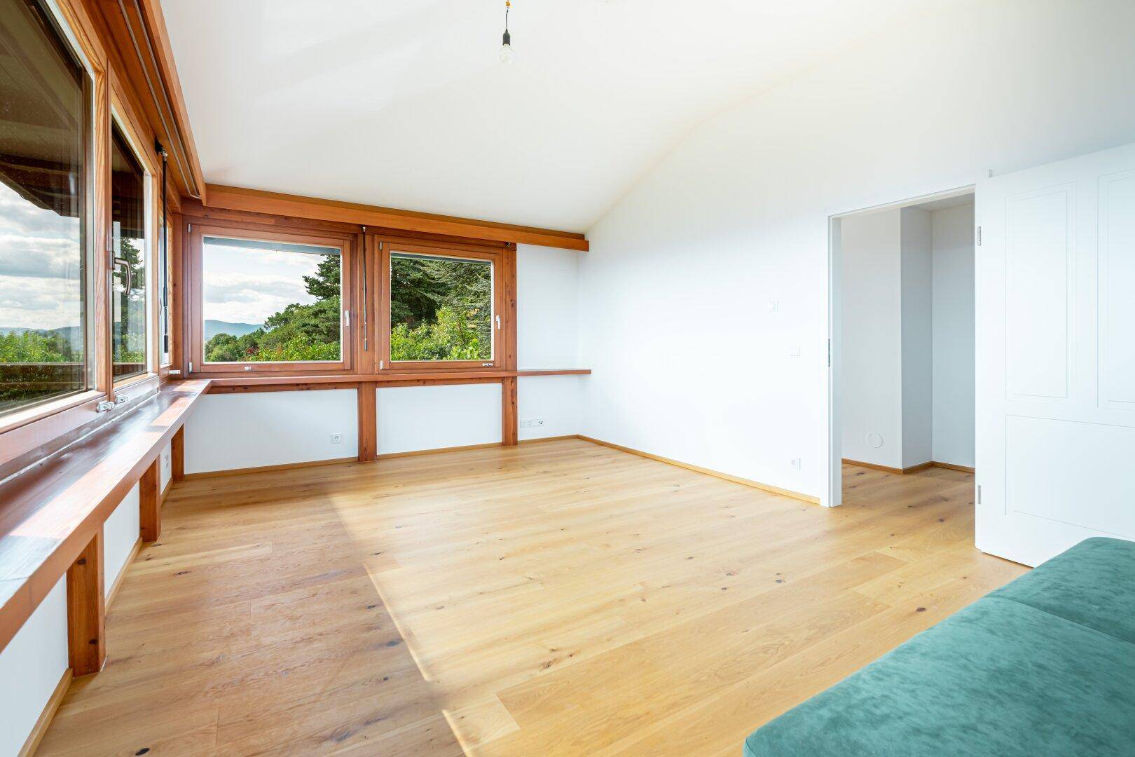 Geräumiges, helles Schlafzimmer mit Holzboden und großen Fenstern, die einen weiten Ausblick bieten.