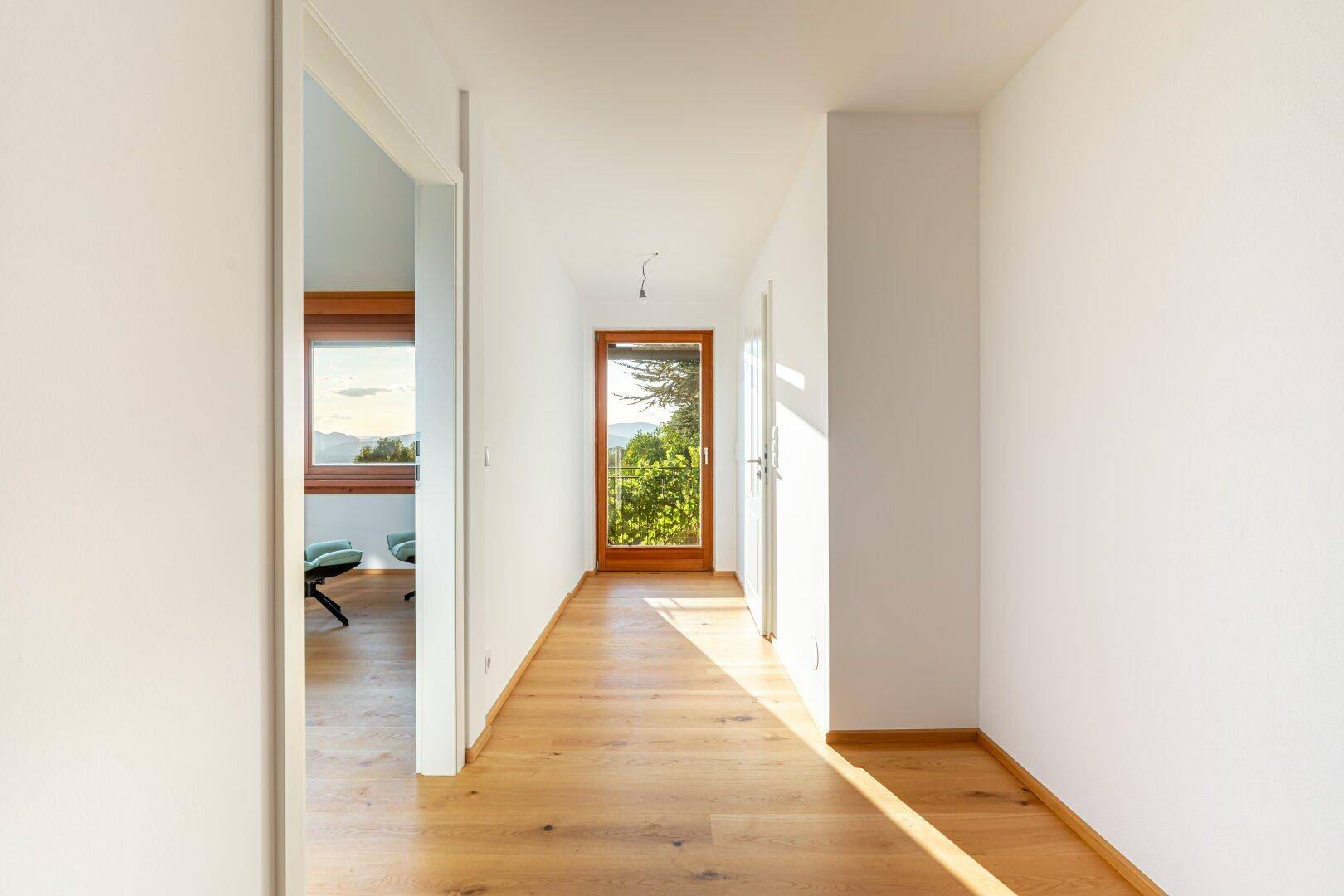 Langer, heller Flur mit Holzboden und Fenstern am Ende, die viel Tageslicht hereinlassen.
