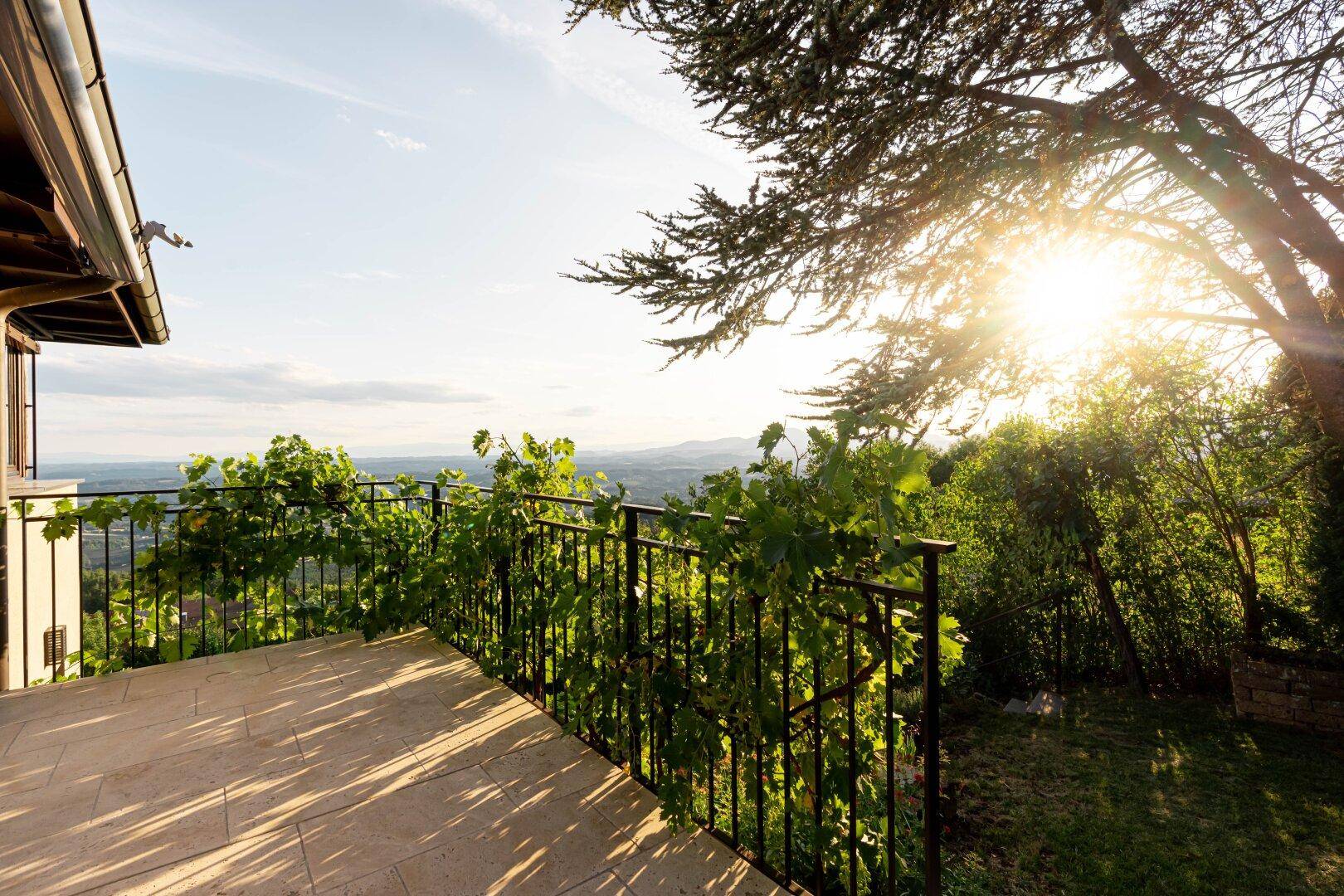Helle Terrasse mit Fliesenboden, umranktem Geländer und weitem Blick in die Landschaft bei Sonnenuntergang.