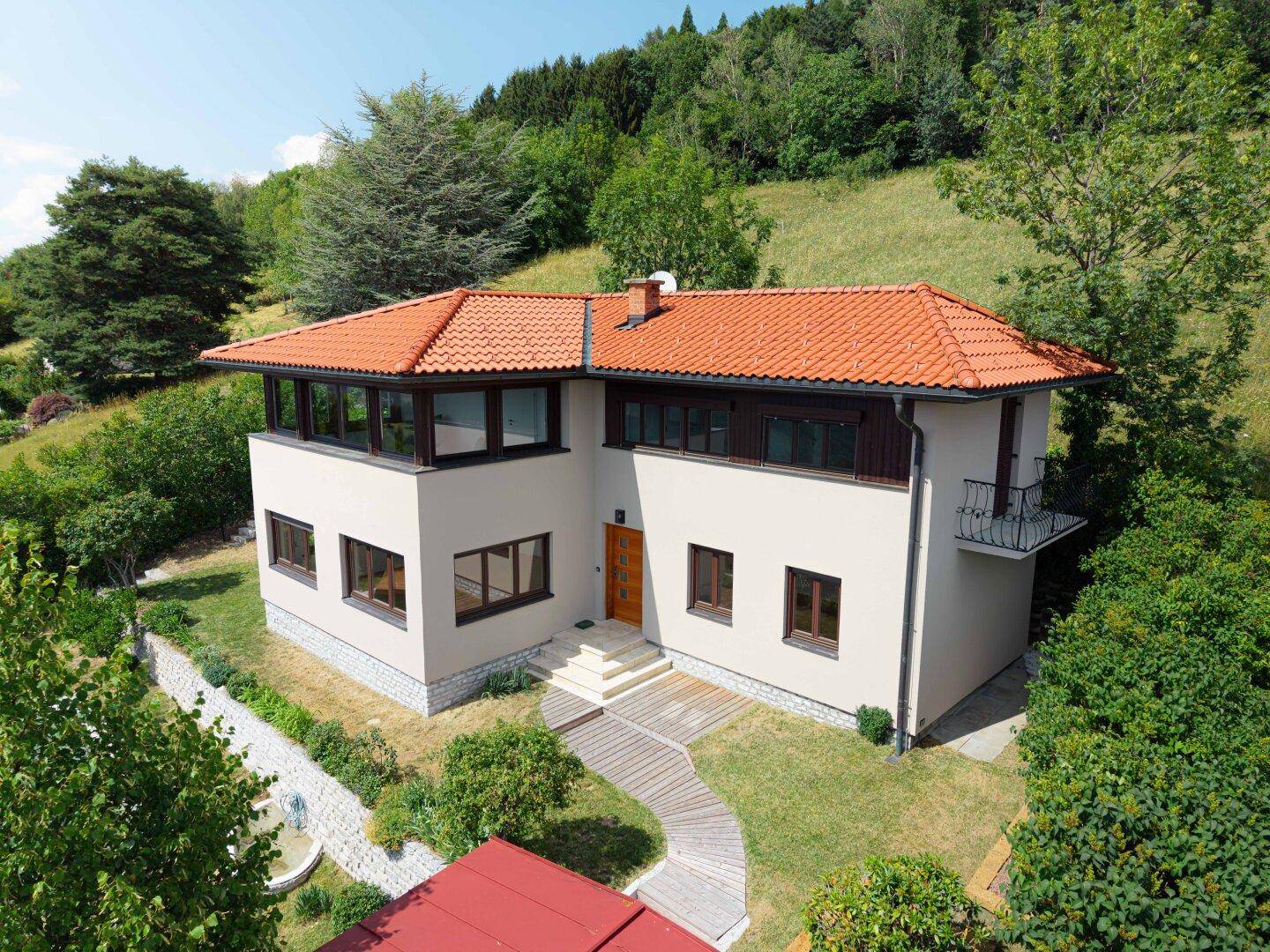 Moderne Hausfassade mit großen Fenstern, Holzeingangstür und einem kleinen Balkon.