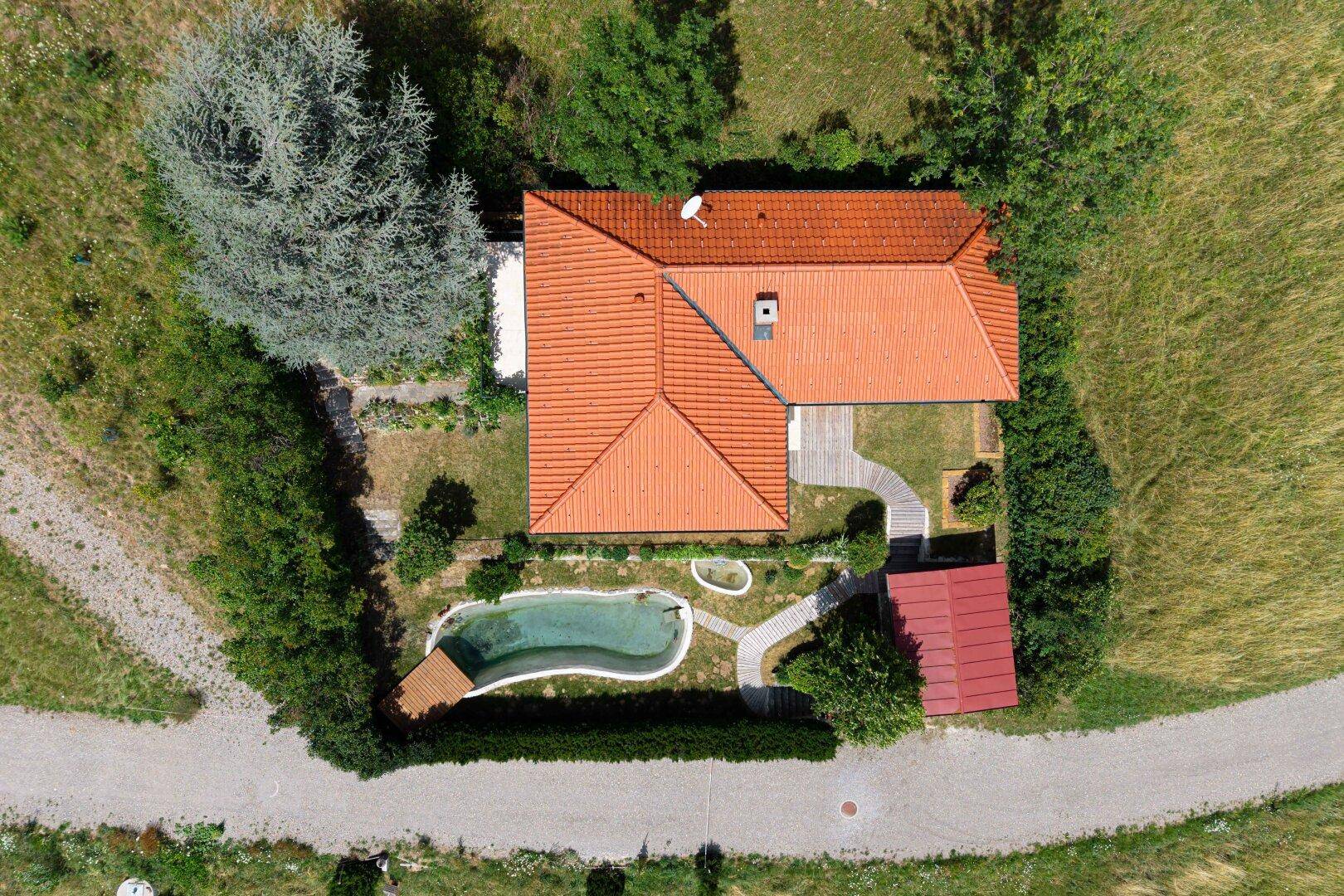 Draufsicht auf ein Haus mit rotem Ziegeldach, Poolbereich und gepflegtem Garten mit Wegen.