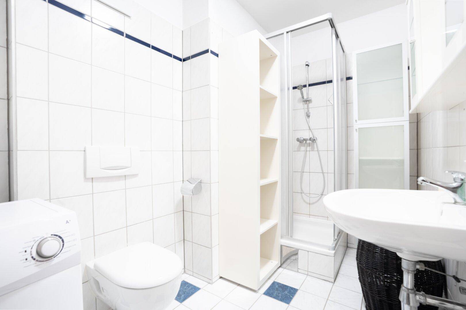 Funktionales Badezimmer mit weißen Fliesen, Dusche, Toilette und Waschmaschine, praktisch eingerichtet.
