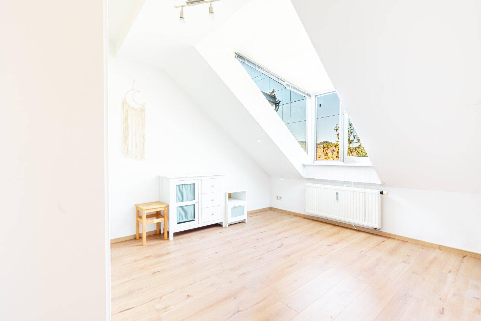 Helles Zimmer mit Dachschrägen, großem Fenster und Holzboden, vielseitig nutzbar als Schlaf- oder Arbeitszimmer.