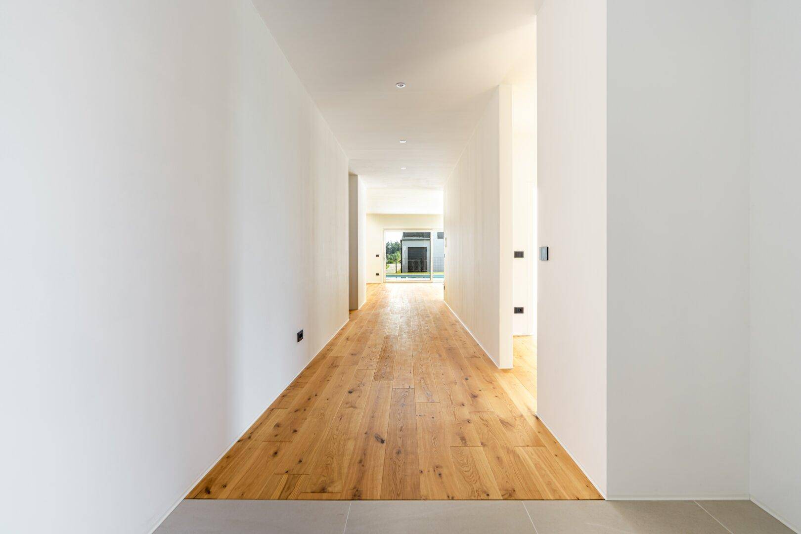 Langer, heller Flur mit Holzboden, der zu weiteren Räumen und dem Außenbereich führt.