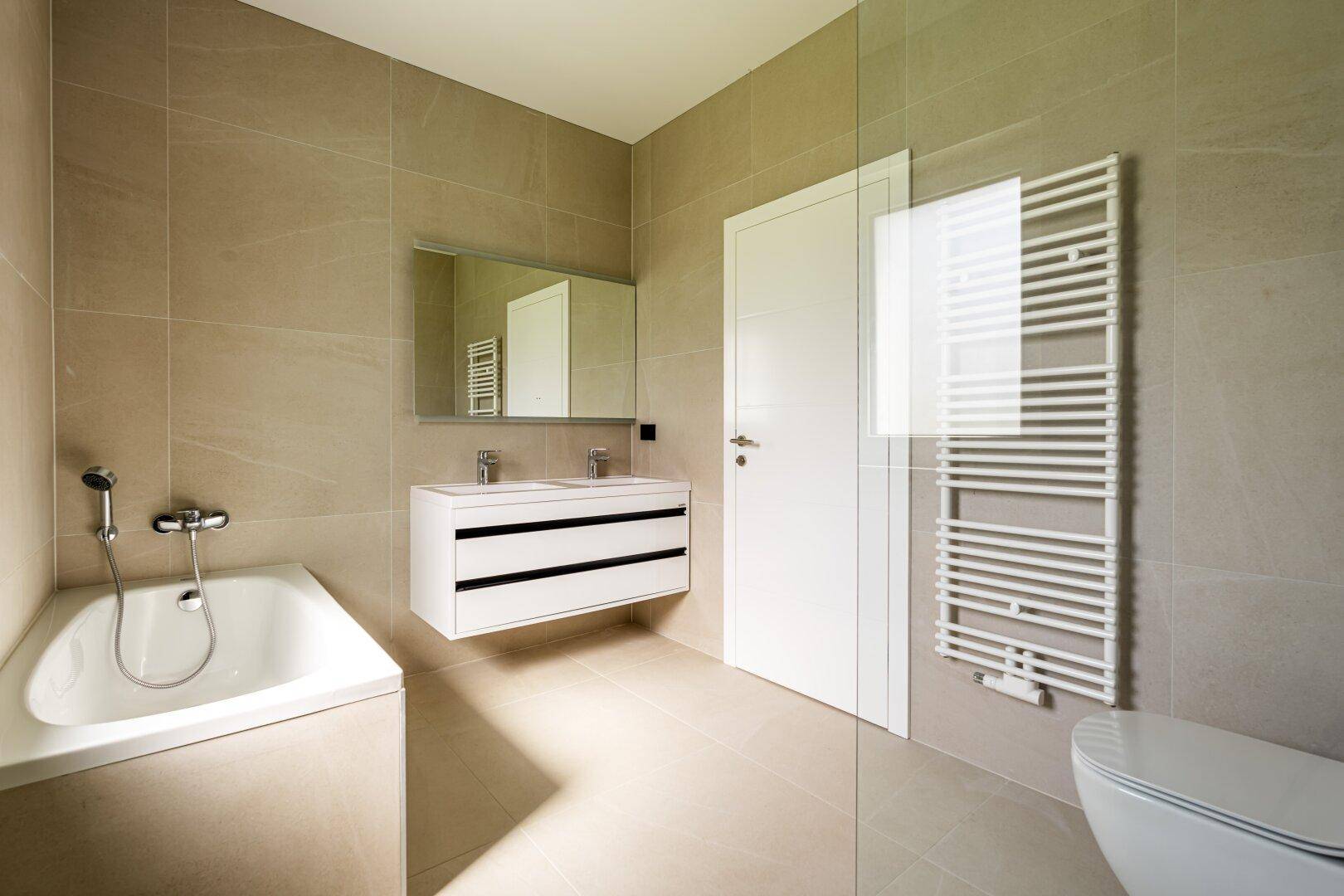 Modernes Badezimmer mit Badewanne, Doppelwaschbecken, beheiztem Handtuchhalter und Dusche.