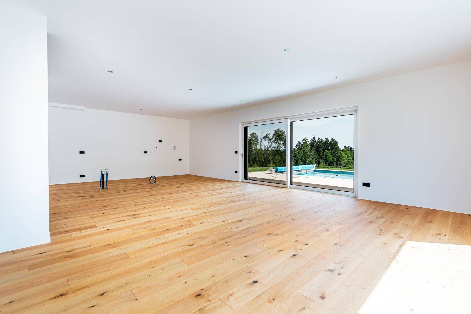 Großer, offener Raum mit Holzboden und Blick auf den Pool, bereit für die Kücheninstallation.