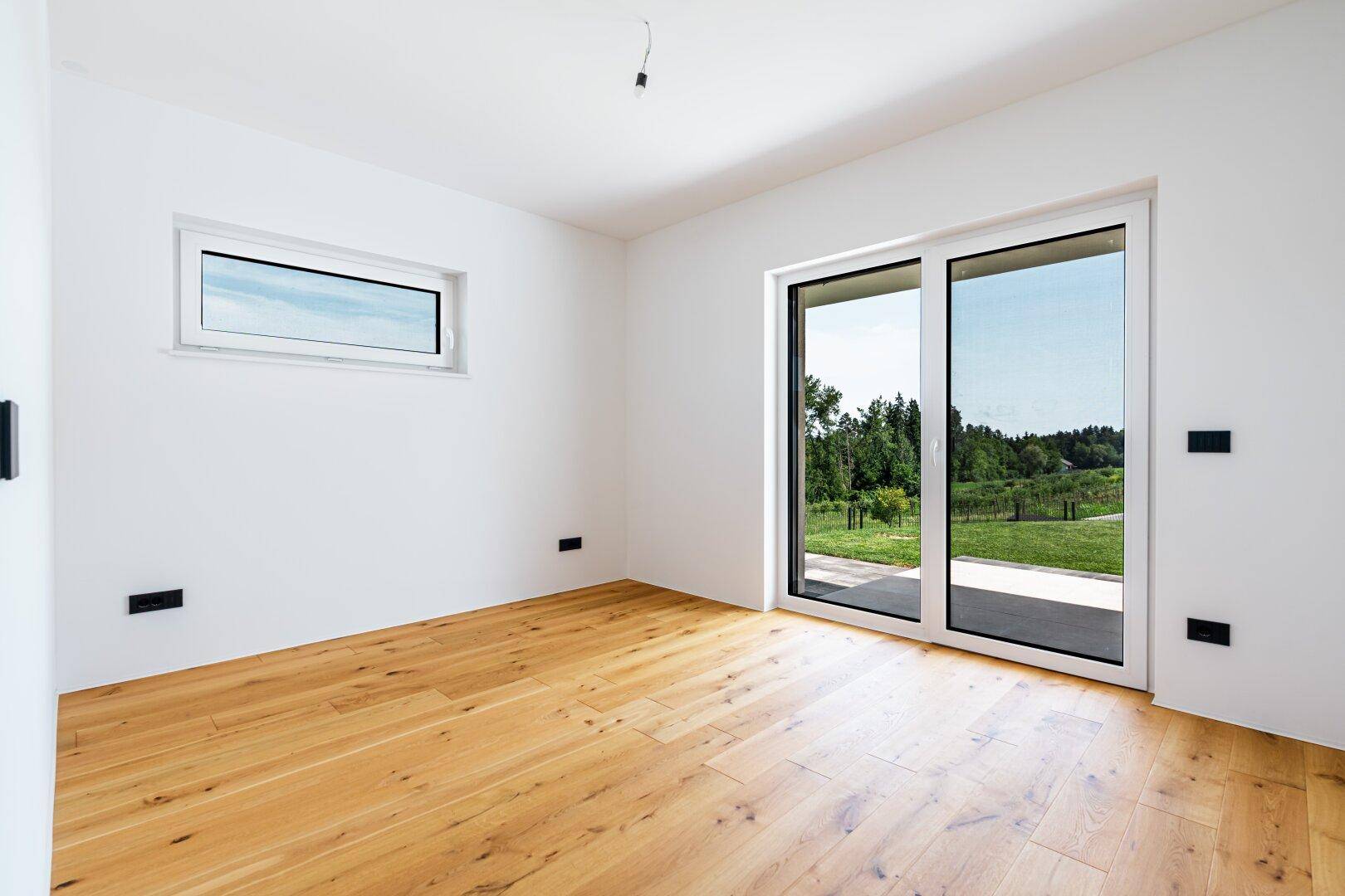Heller Raum mit Holzboden und großer Schiebetür zum Garten, ideal als Schlaf- oder Arbeitszimmer.