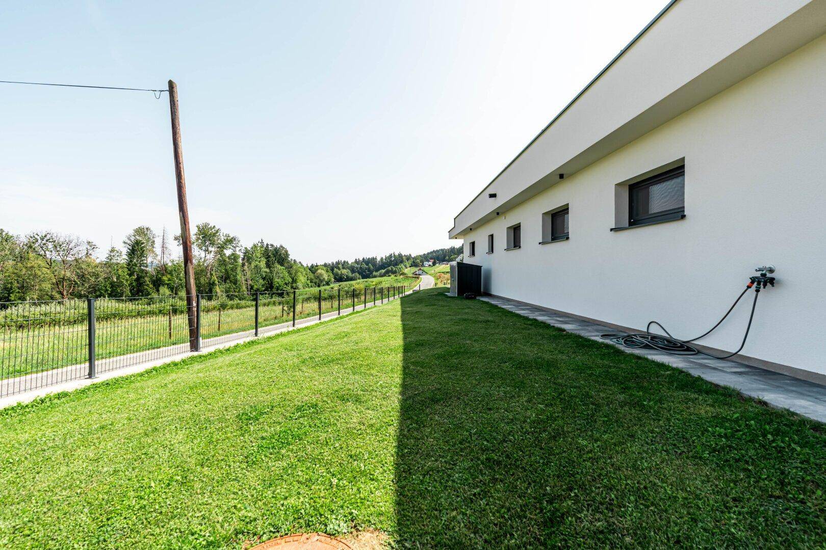 Seitenansicht des Hauses mit gepflegtem Rasen und Blick auf die umliegende Natur.