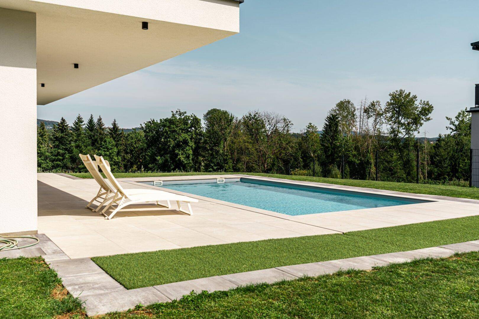 Entspannender Poolbereich mit Liegestühlen und Blick ins Grüne, umgeben von einer hellen Terrasse.