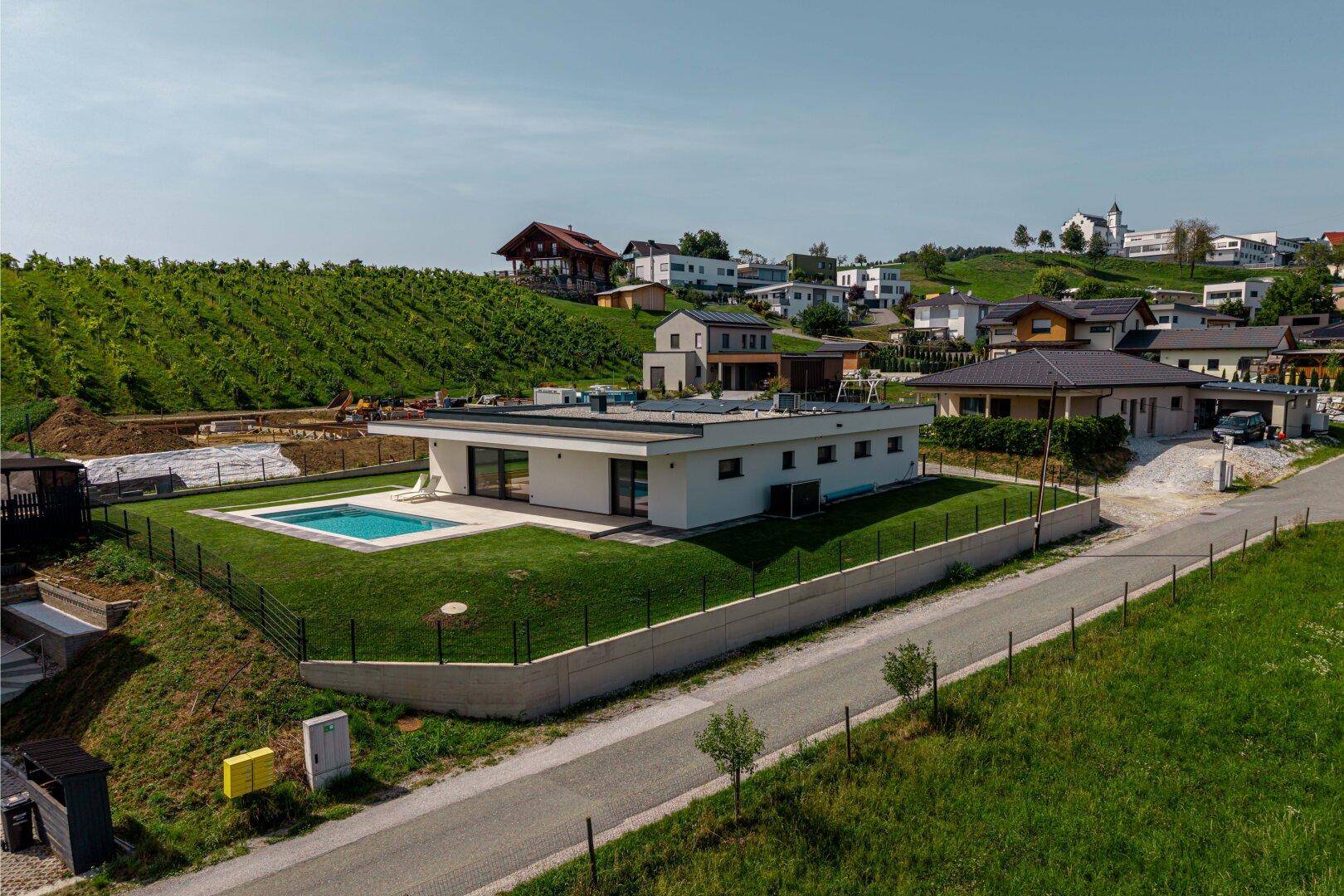 Luftaufnahme eines modernen Hauses mit Pool, umgeben von Weinbergen und ländlicher Bebauung.