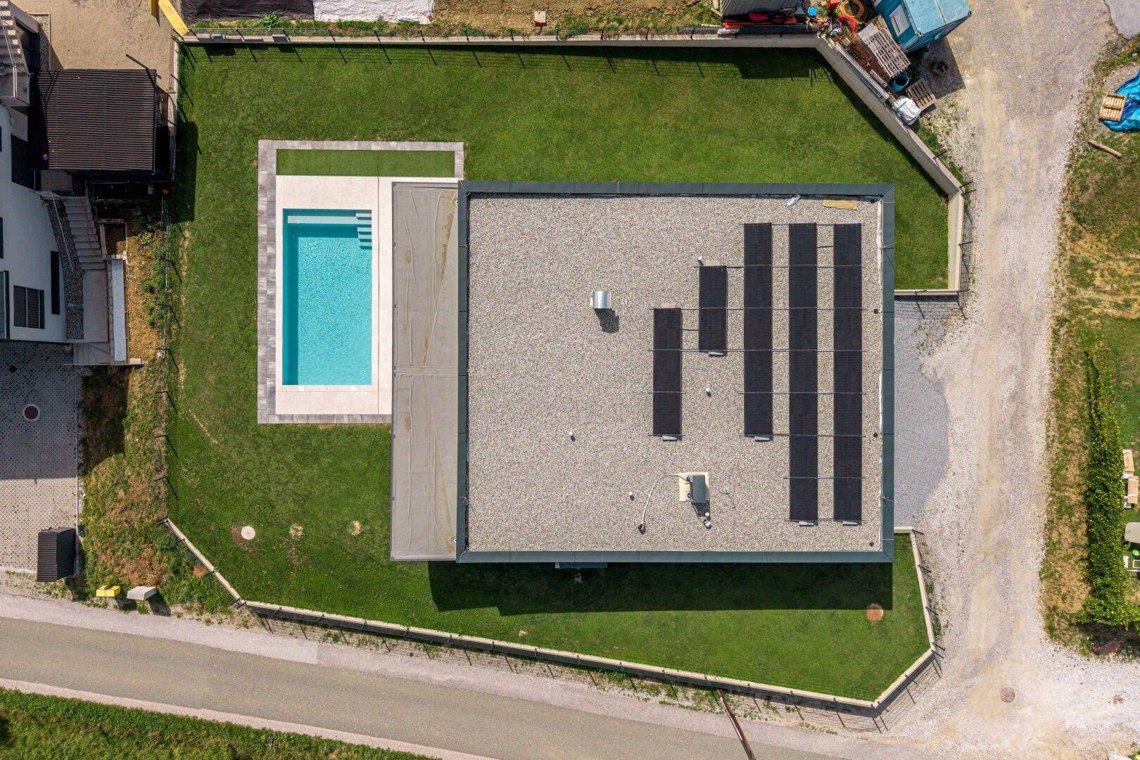 Draufsicht auf das moderne Haus mit Flachdach, Photovoltaikanlage und Swimmingpool im Garten.