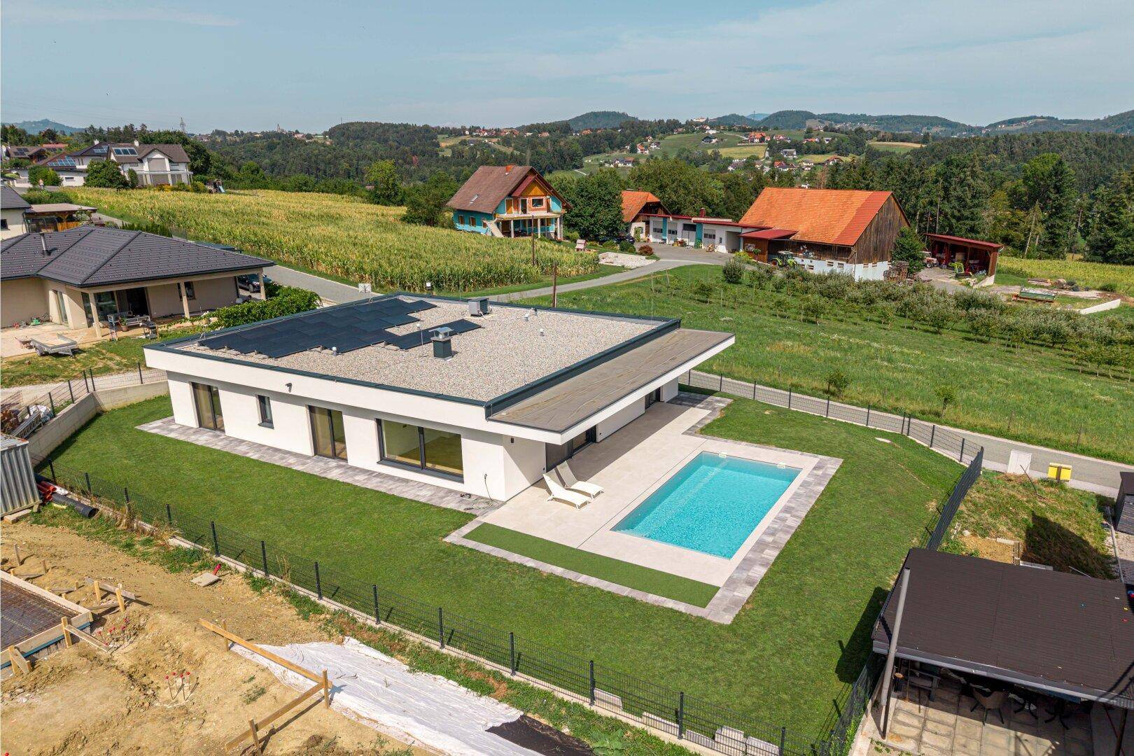 Weitläufige Ansicht des modernen Hauses mit Pool, umgeben von grüner Landschaft und anderen Häusern.