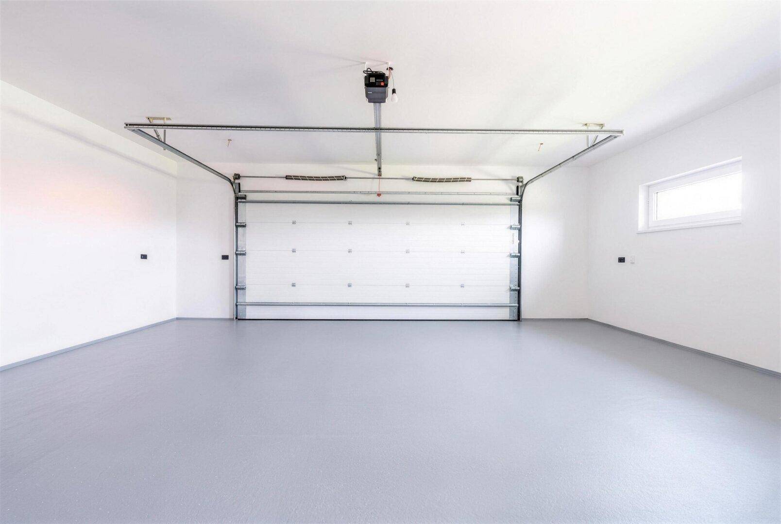 Geräumige Garage mit automatischem Tor, hellem Boden und einem Fenster.