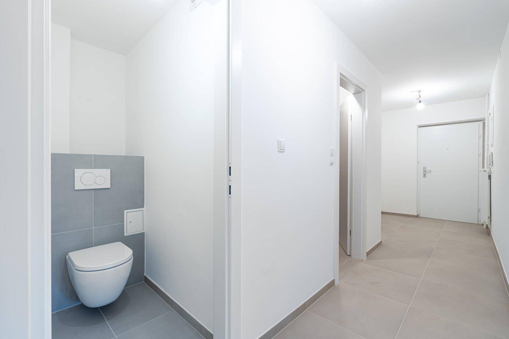 Heller Flur mit Zugang zu einem modernen Gäste-WC mit Wand-WC und Fliesen.