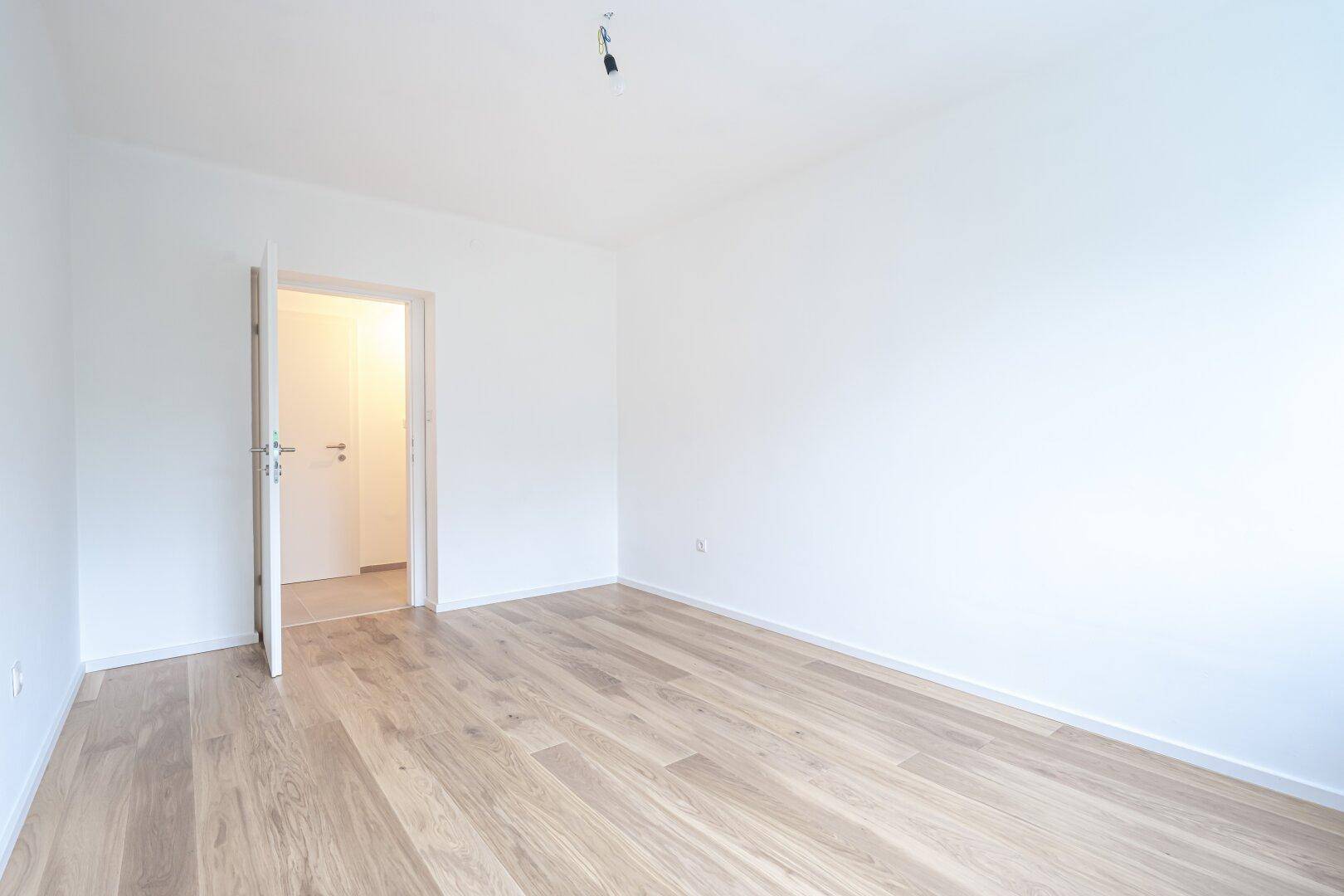 Unmöbliertes Schlafzimmer mit hellem Holzboden und offener Tür zu einem angrenzenden Bereich.