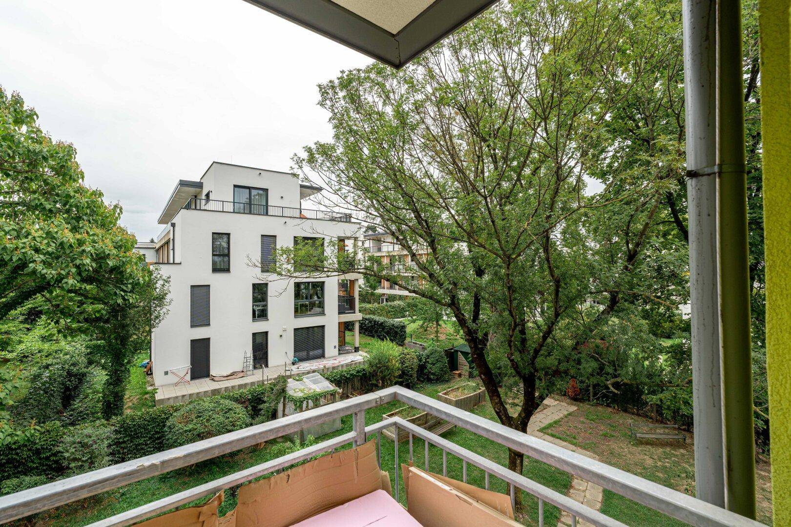 Balkon mit Blick auf einen gepflegten Gartenbereich und angrenzende moderne Wohngebäude.