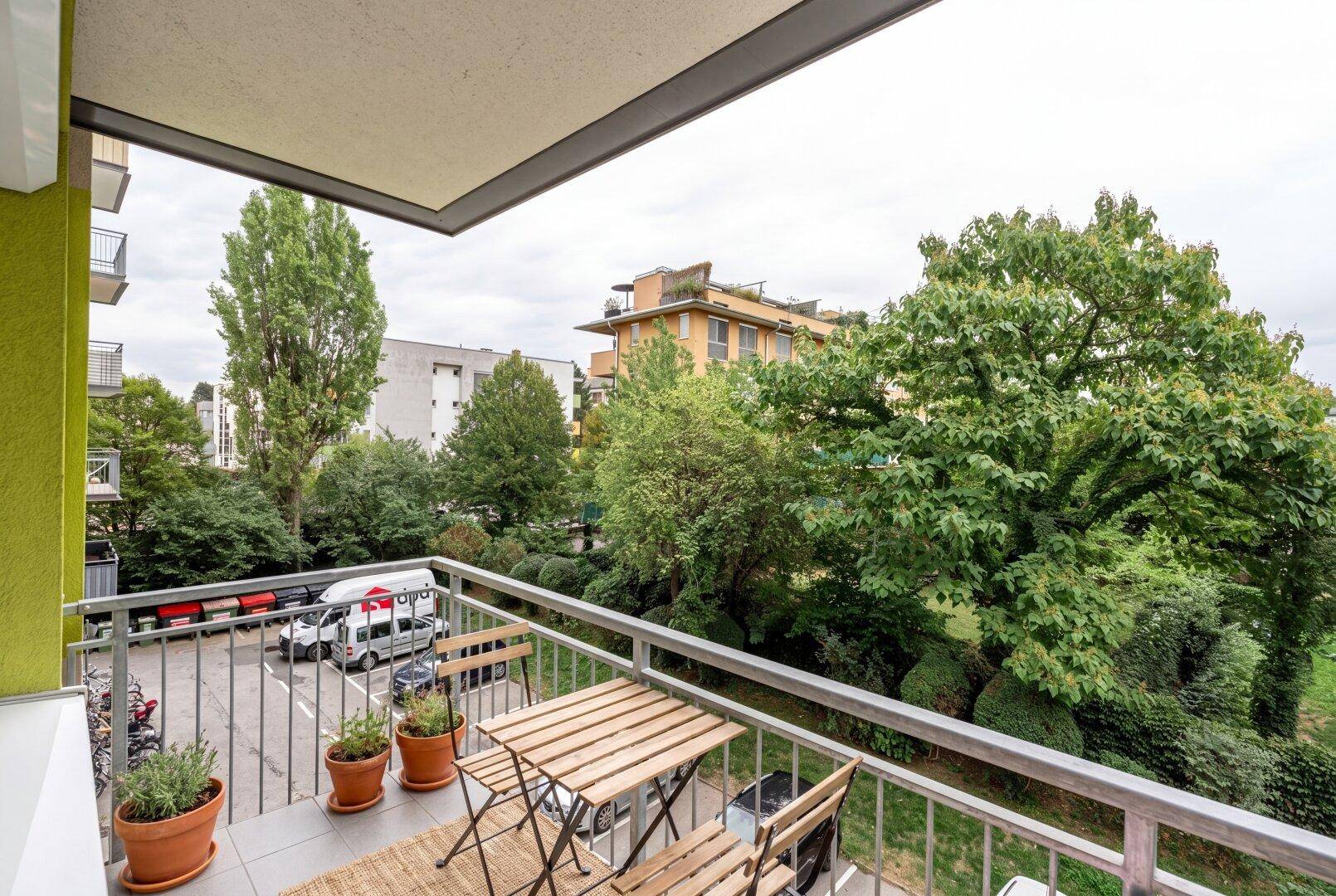 Gemütlicher Balkon mit Holztisch und Stühlen, umgeben von Bäumen und Blick auf die Umgebung.