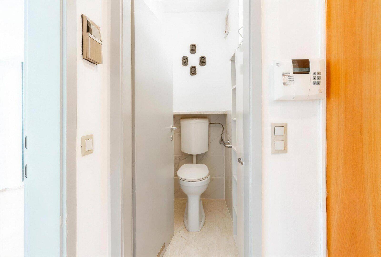 Kleines Gäste-WC mit Toilette und hellen Fliesen, funktional eingerichtet.