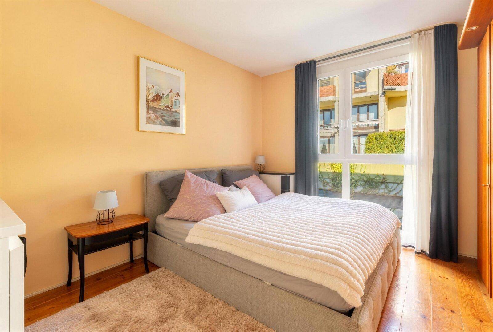 Helles Schlafzimmer mit Doppelbett, Teppich und großem Fenster mit Blick nach draußen.